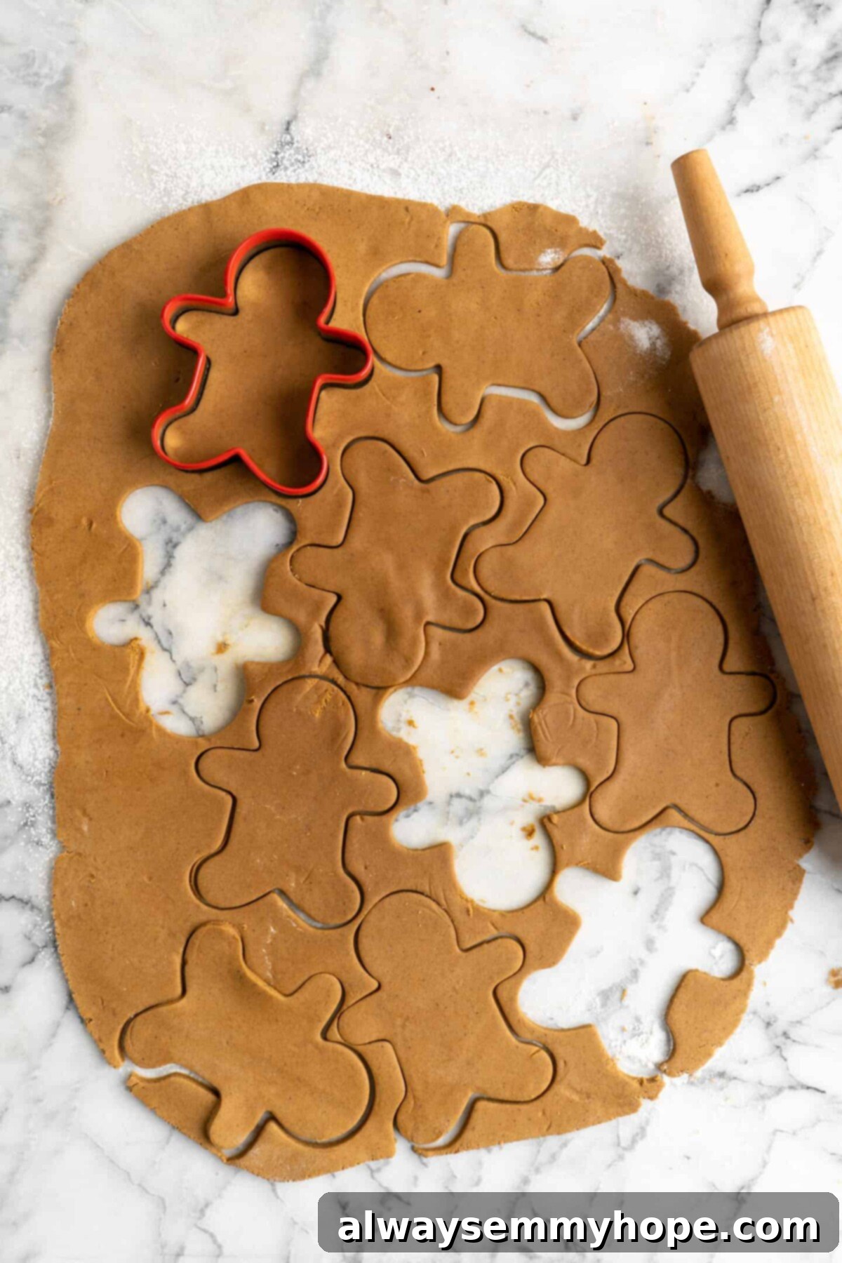 Rolled out gingerbread men dough with marks for a lot of gingerbread men to be cut out, and three gingerbread men already cut out, with a cookie cutter on top, and a rolling pin to the side