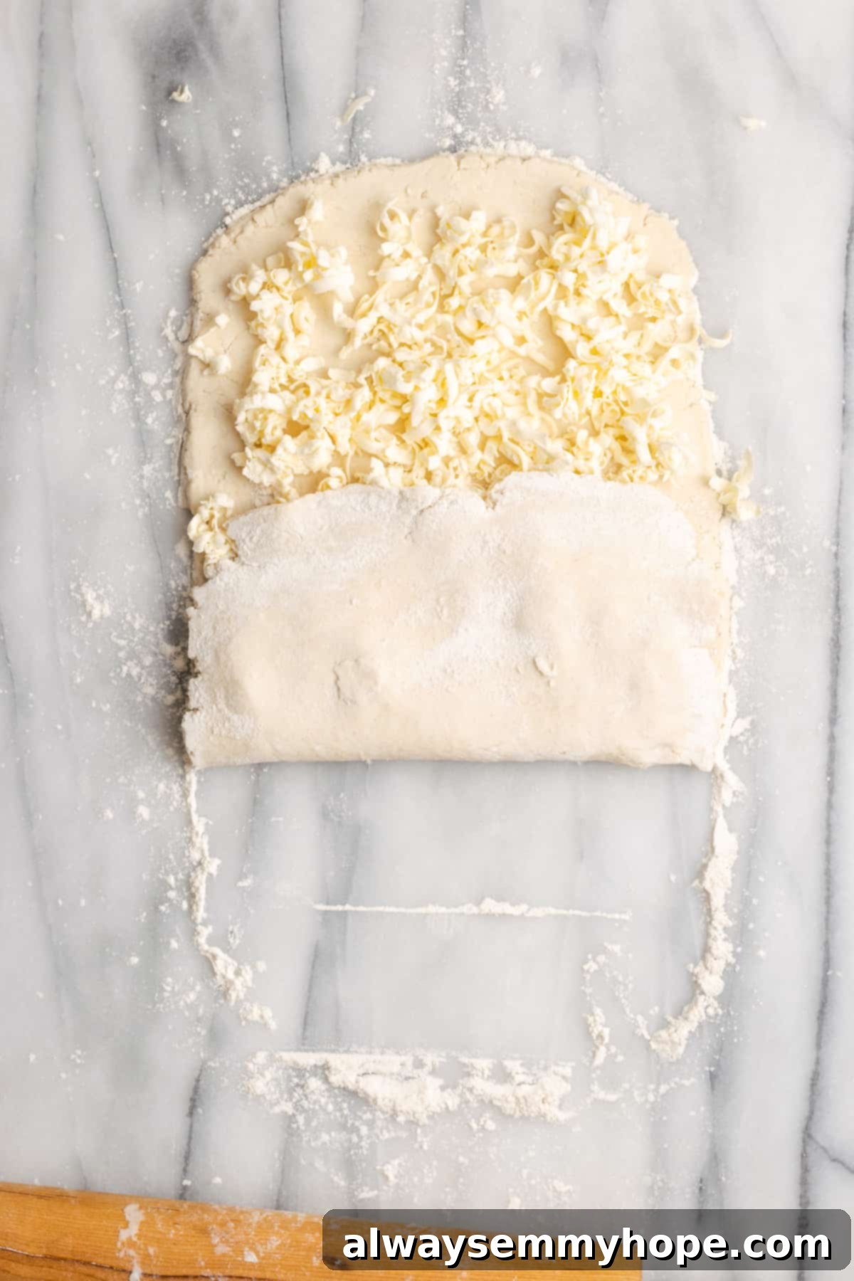 A rectangle of dough with shredded butter on top, with a third of the dough folded up