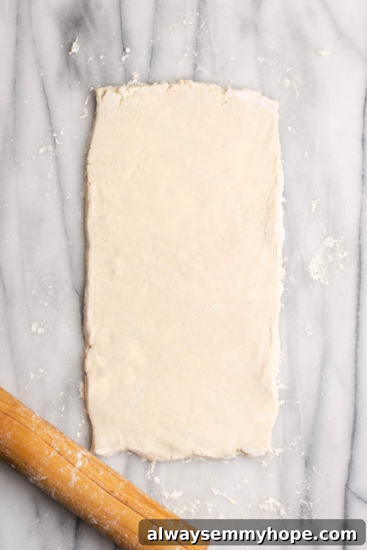 A slightly thick rectangle of dough rolled out next to a rolling pin