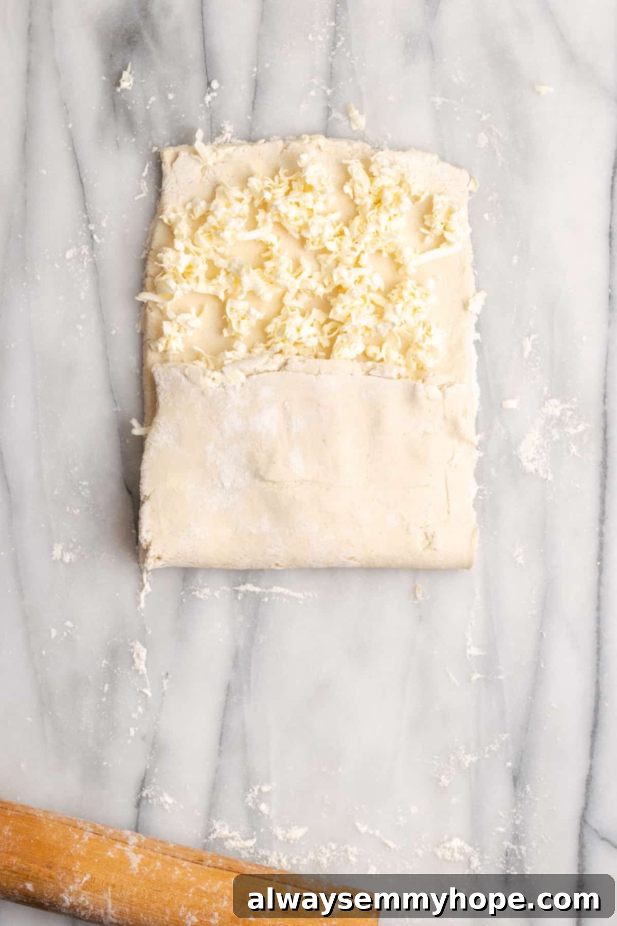 A rectangle of dough with shredded butter on top, with a third of the dough folded up