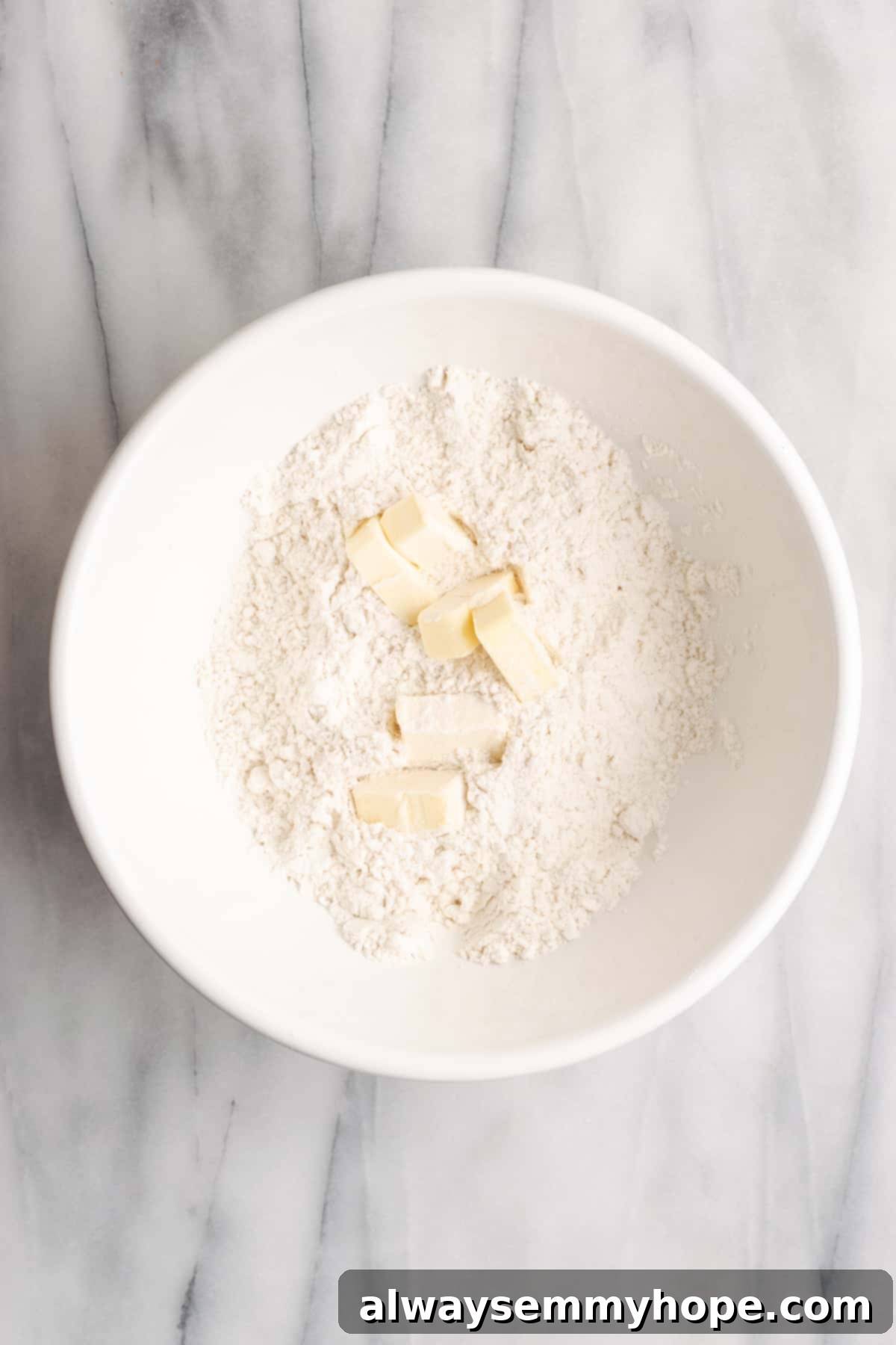 A mixing bowl with flour, salt, sugar, and chunks of vegan butter