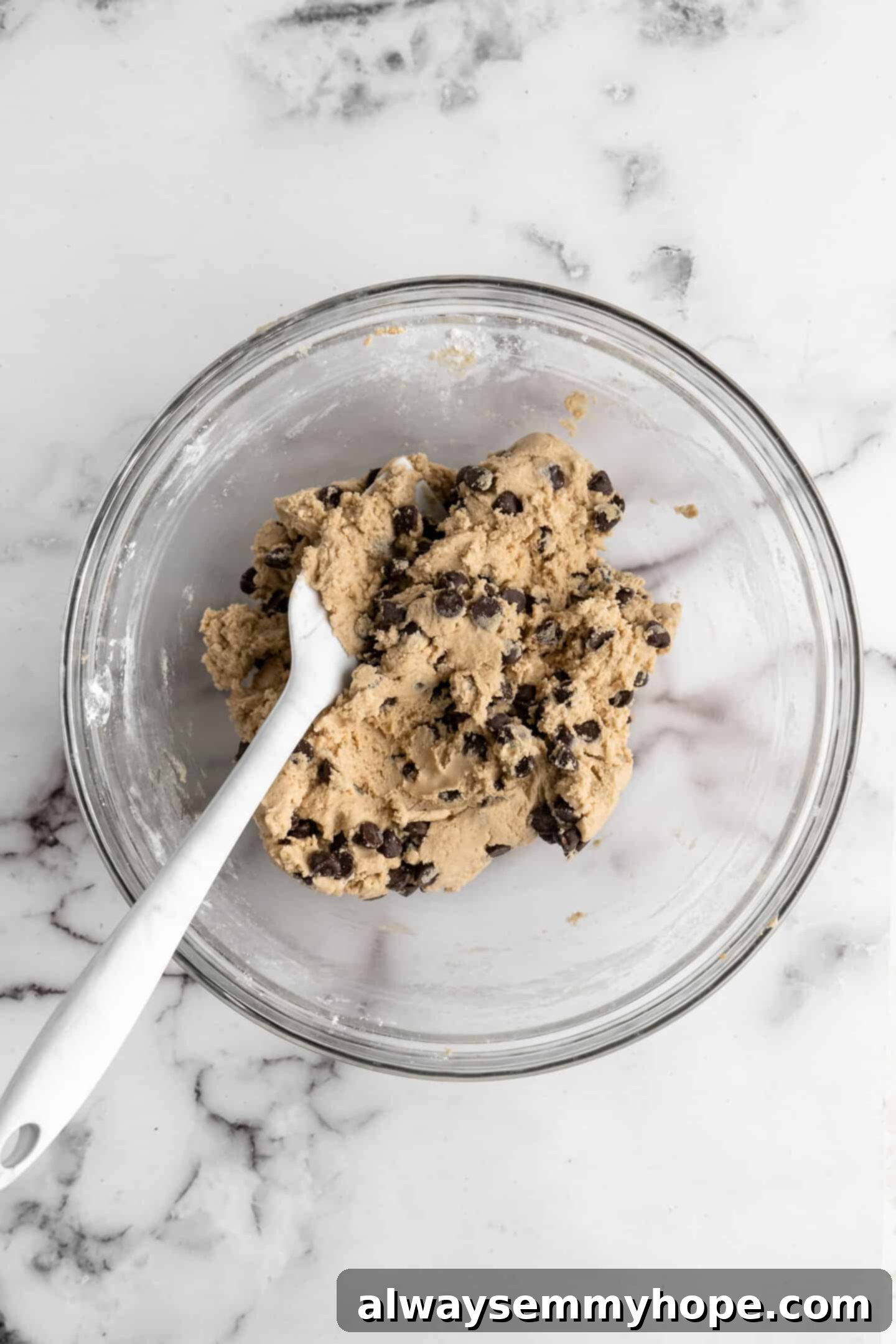 Finished chocolate chip cookie dough in a glass bowl with a spatula, ready for chilling