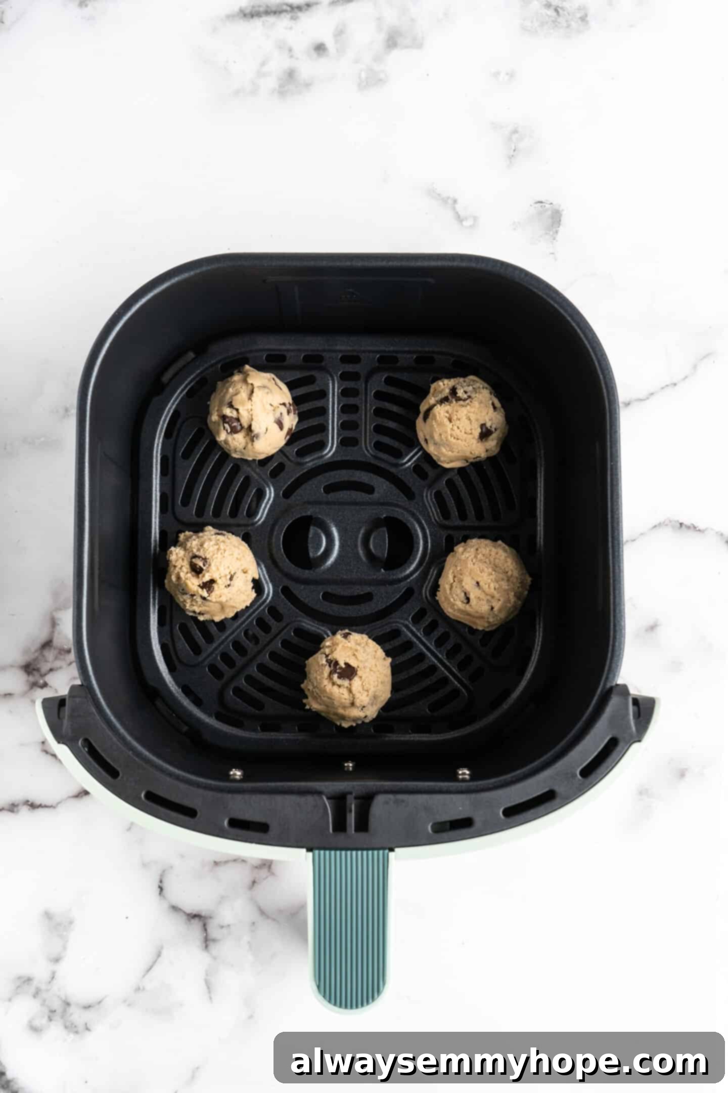 Scooped balls of chocolate chip cookie dough neatly arranged in the base of an air fryer basket, ready for baking