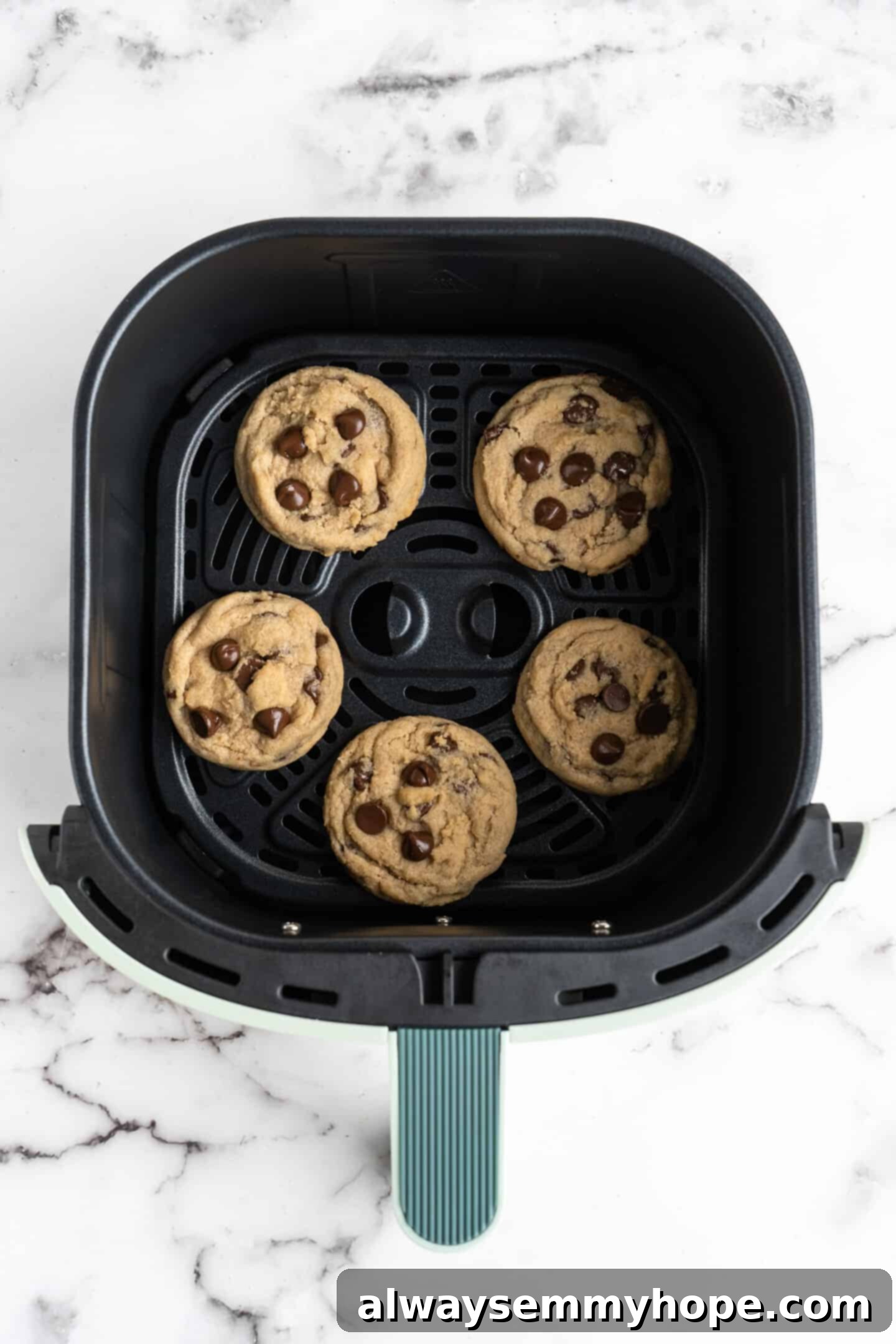 Perfectly baked air fryer chocolate chip cookies sitting in the air fryer base, golden brown and slightly crisp