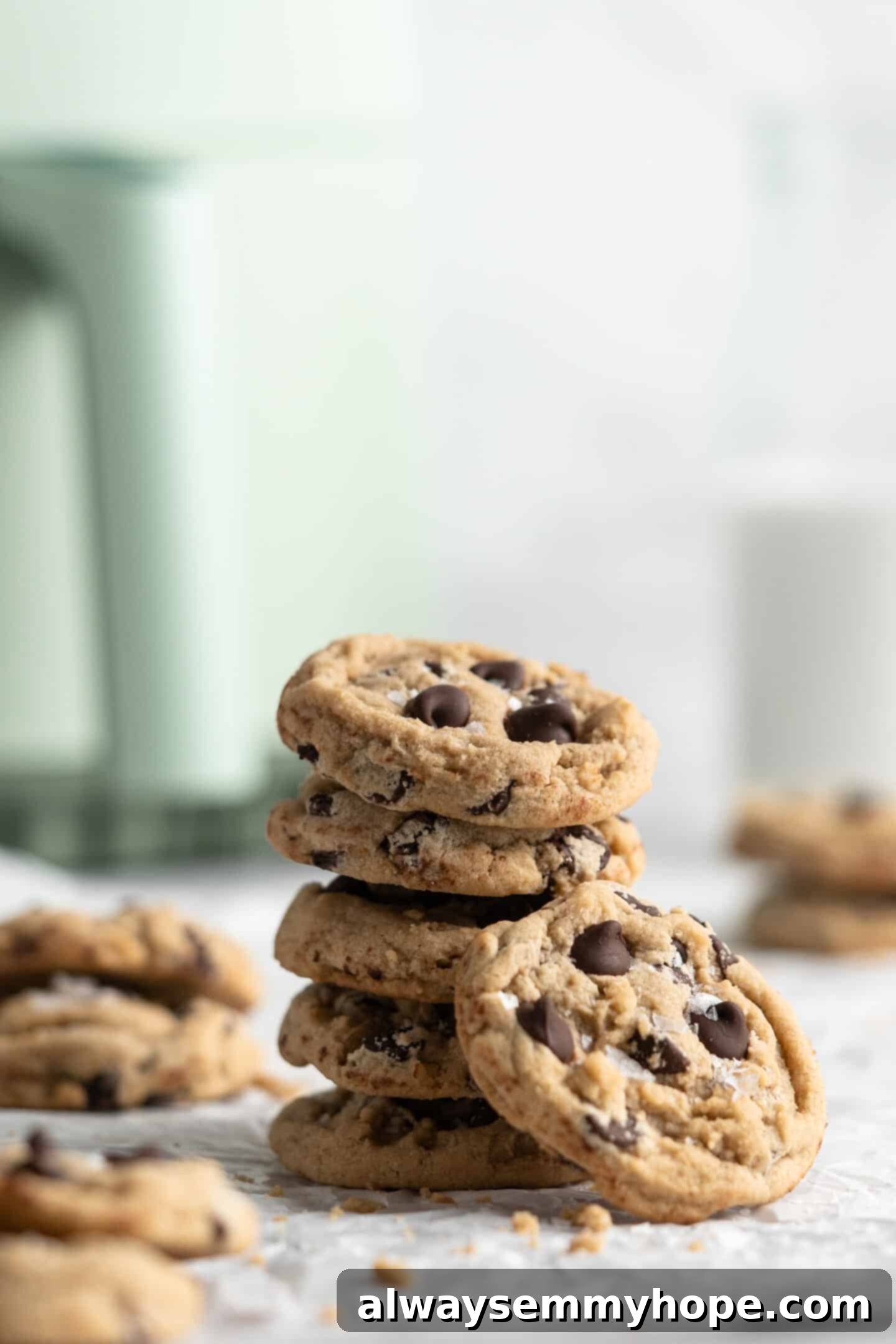 Stack of freshly baked vegan chocolate chip cookies, with a pitcher of vegan milk and the teal air fryer visible in the blurred background