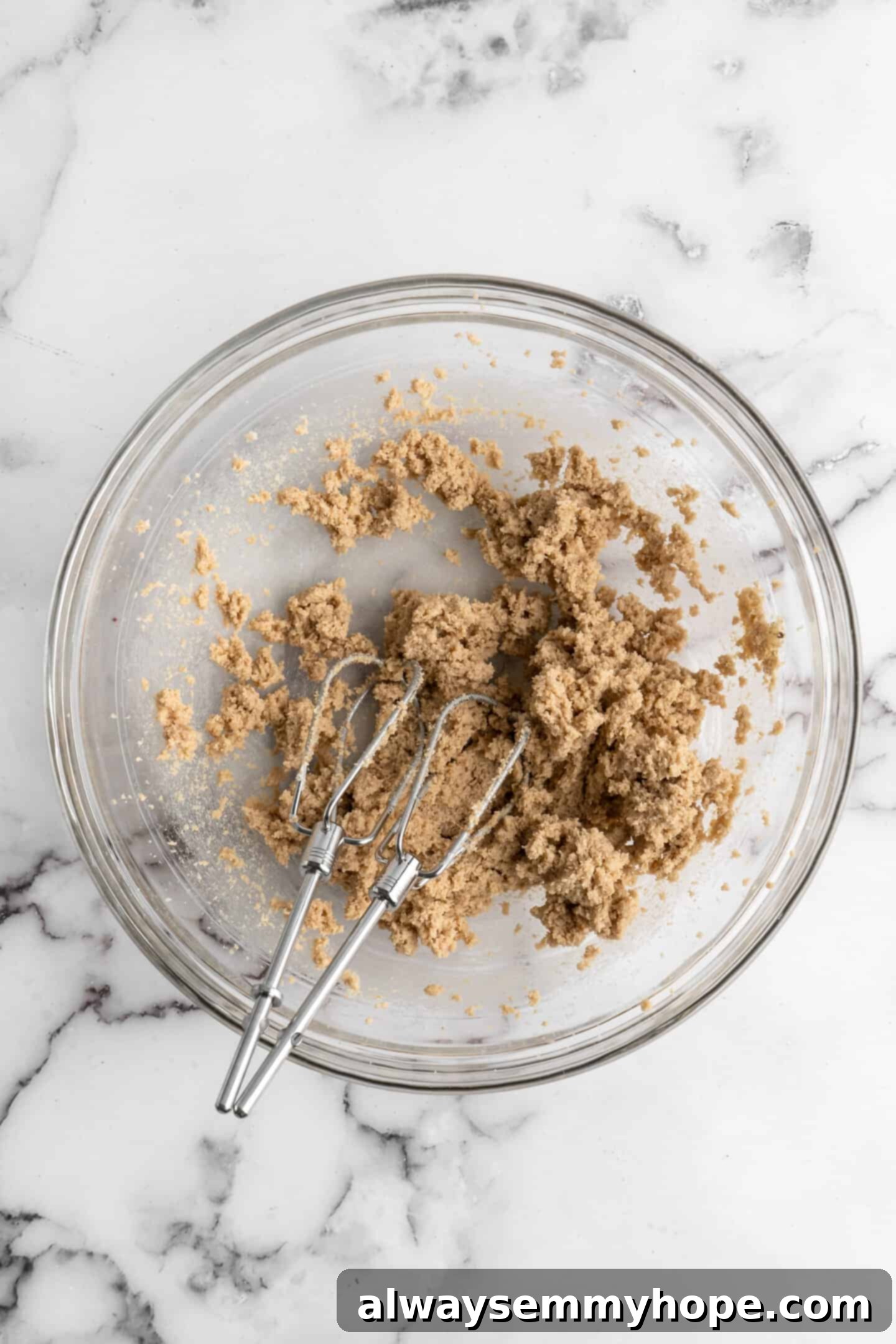 Overhead view of creamed vegan butter and sugars in a glass bowl with a whisk, showing a light and fluffy texture