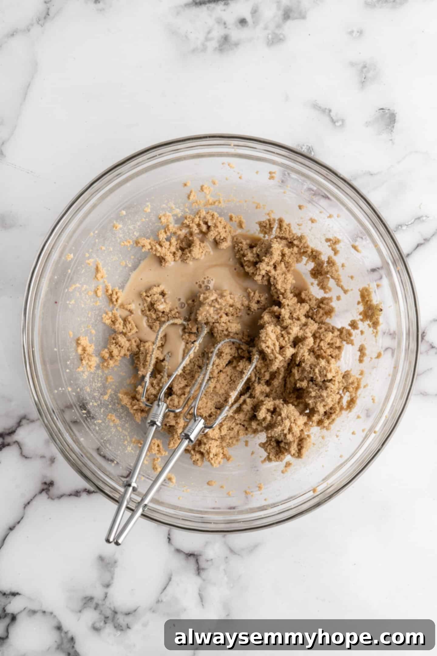 Overhead view of creamed wet ingredients with vegan milk added, being mixed further in a glass bowl with a whisk