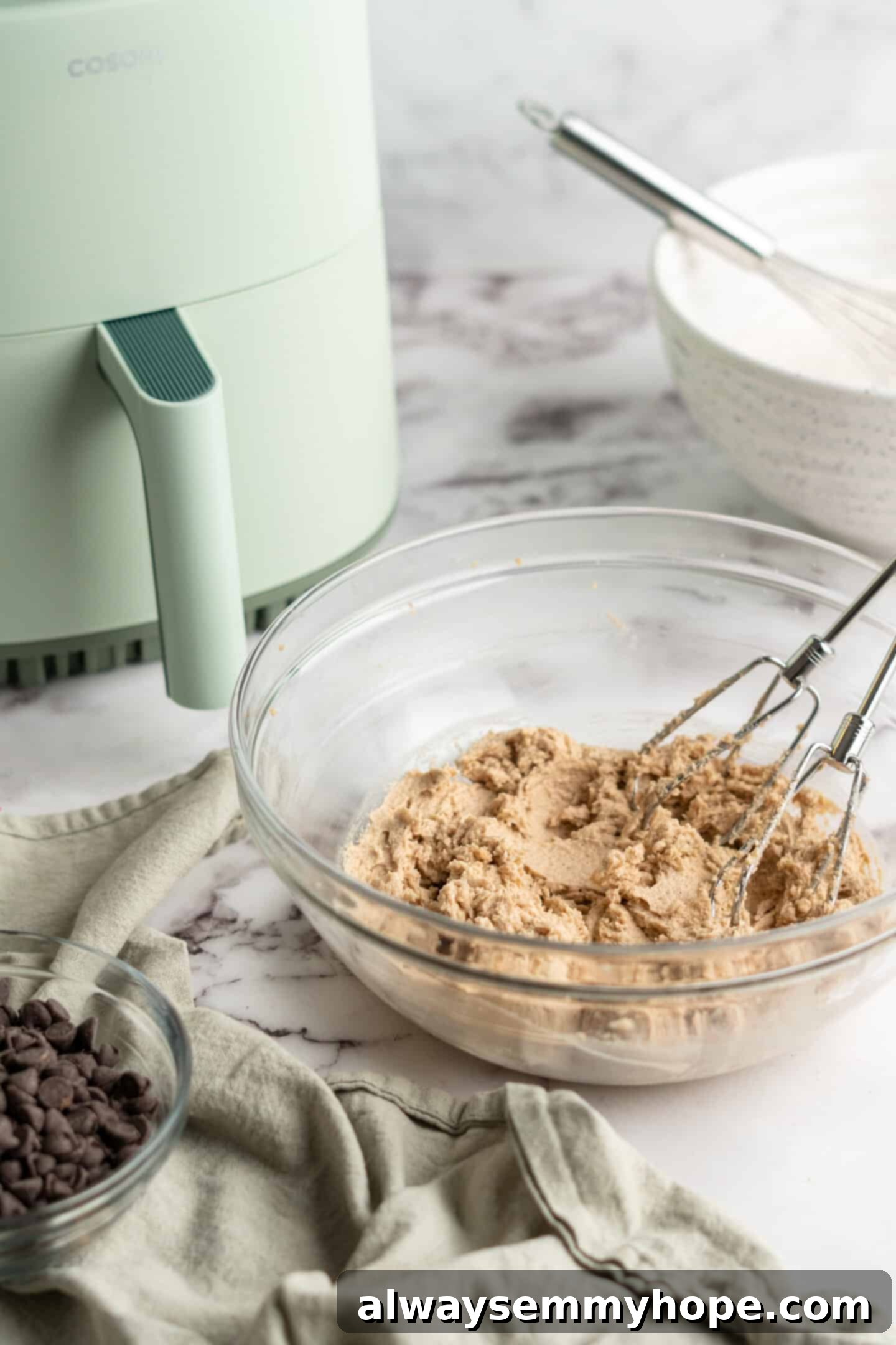 Overhead view of fully mixed cookie dough in a mixing bowl, with the Cosori air fryer visible in the background