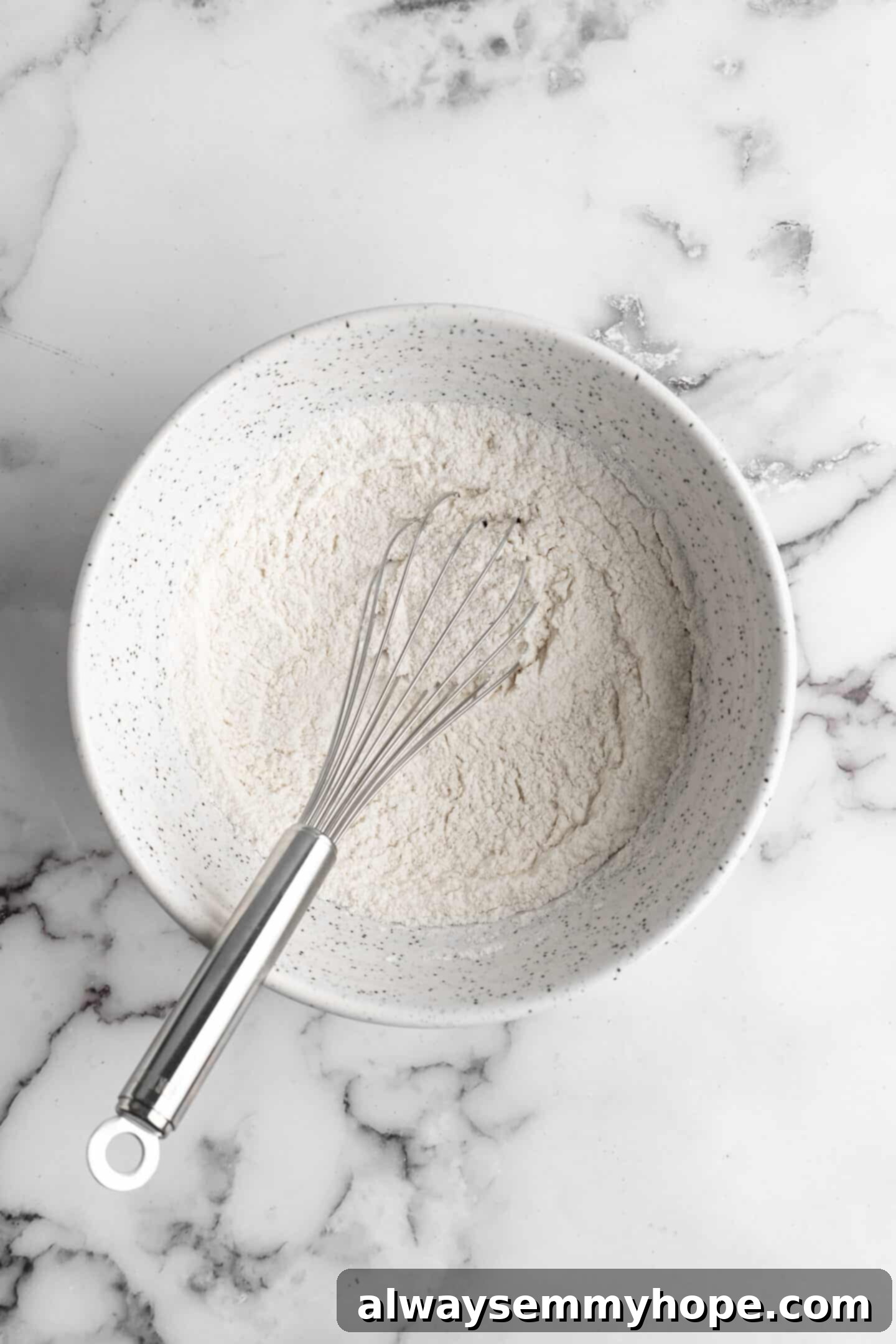 Overhead view of dry cookie ingredients (flour, cornstarch, baking soda, salt) expertly whisked together in a separate glass bowl