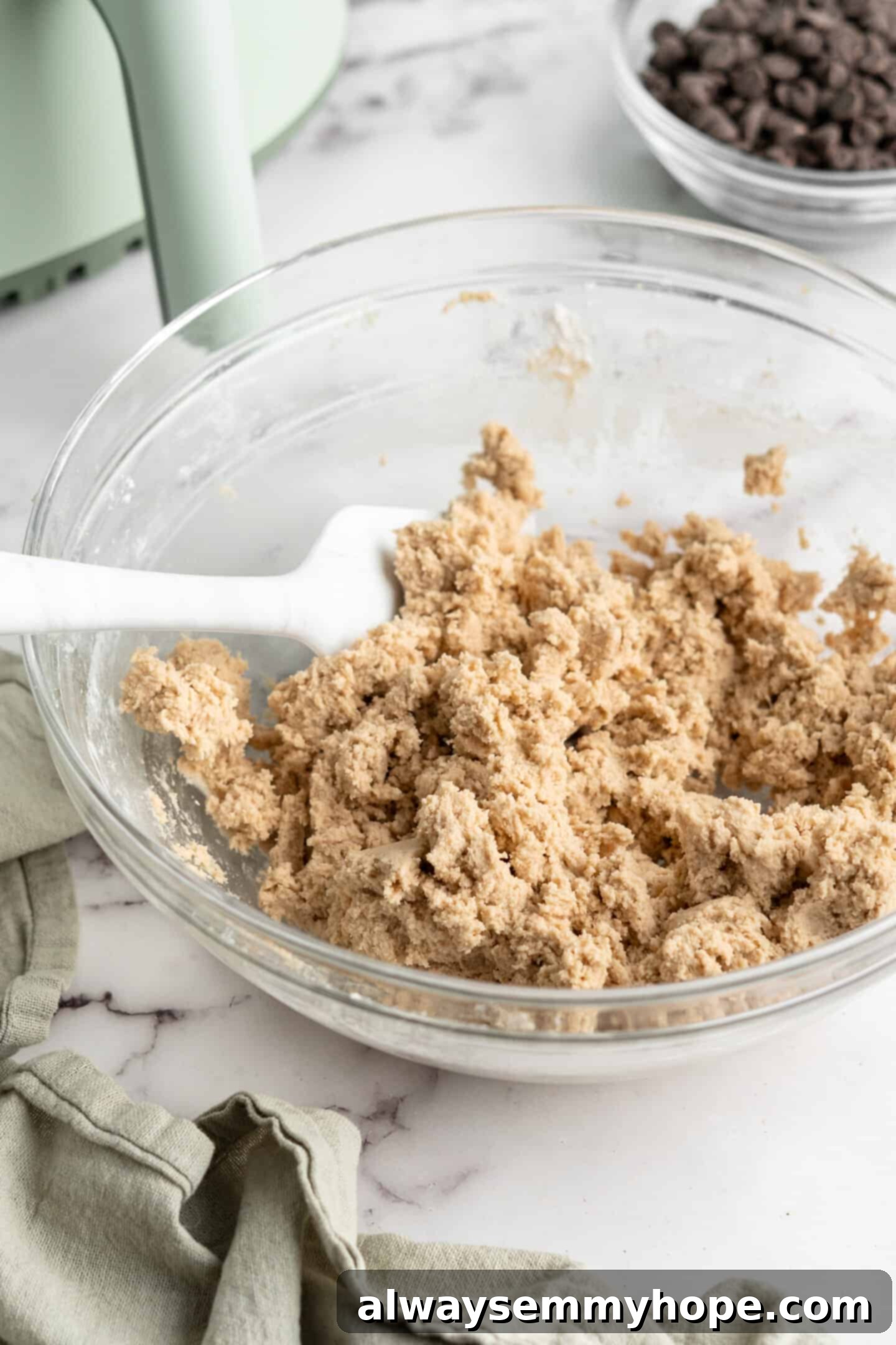 Cookie dough in glass mixing bowl with spatula, showing the transition from dry to wet ingredients