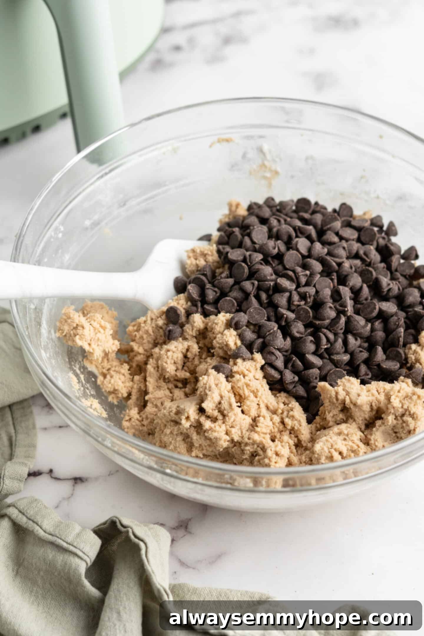 Cookie dough and vegan chocolate chunks being folded together in a glass bowl with a spatula