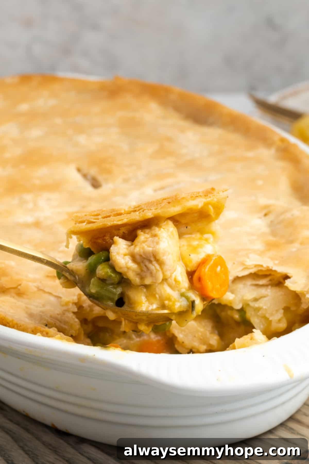 A close-up of a spoonful of creamy vegan chicken pot pie casserole, with the full casserole dish blurred in the background, highlighting its rich texture and golden crust.
