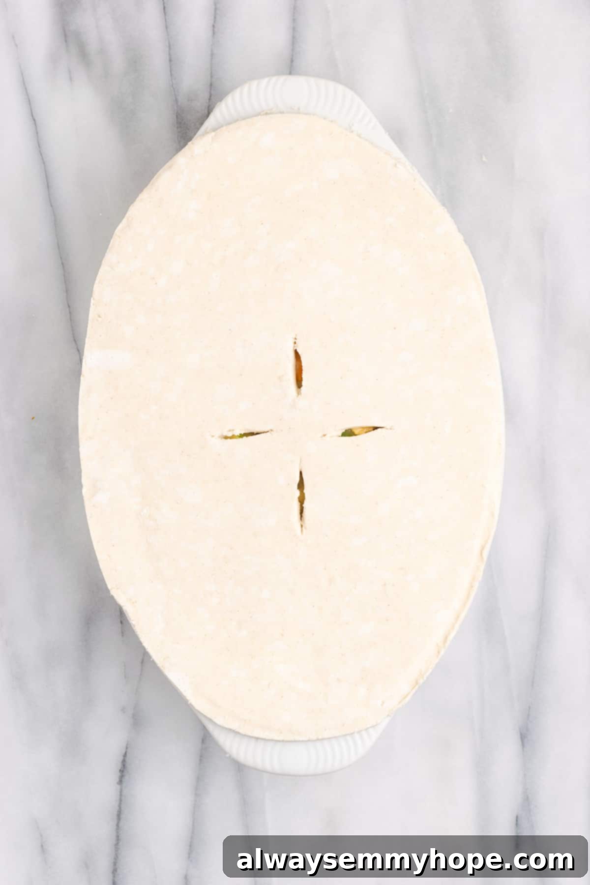 An overhead view of an unbaked vegan pot pie casserole with the puff pastry dough carefully placed on top, vents cut, and ready for the oven.
