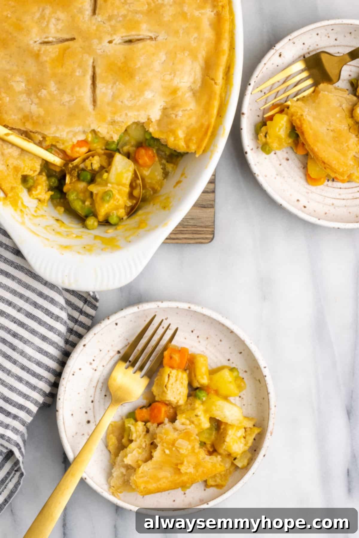 A serving spoon lifting a generous portion of vegan chicken pot pie casserole from the dish, with two plated servings and forks visible beside it, emphasizing its delicious and comforting appeal.