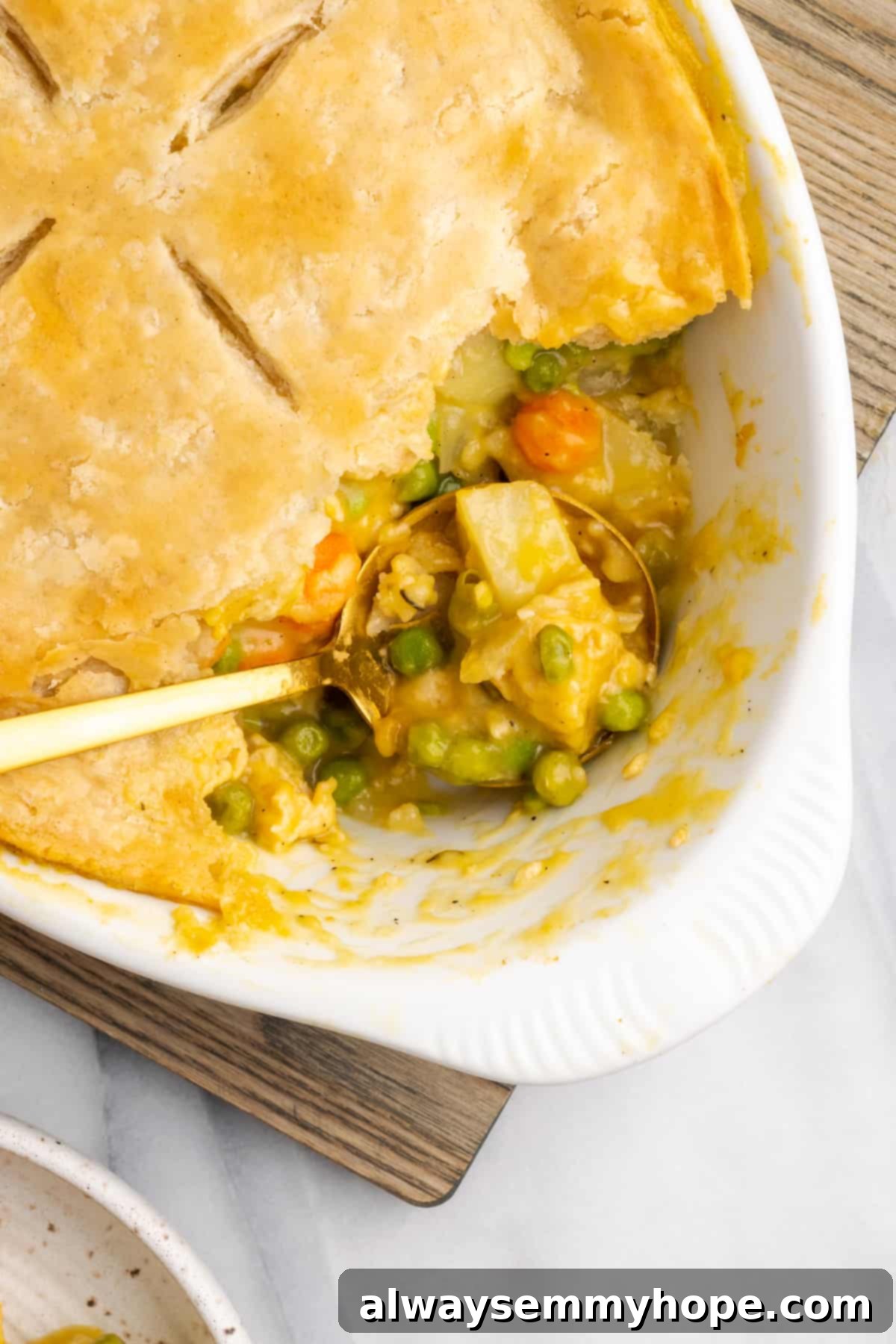 A close-up of a spoon scooping a hearty portion of vegan chicken pot pie casserole out of the warm, golden-crusted dish, emphasizing its rich and comforting texture.