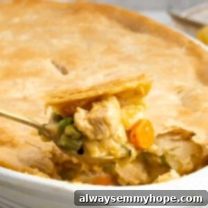 A close-up of a spoonful of creamy vegan chicken pot pie casserole, with the full casserole dish blurred in the background, highlighting its rich texture and golden crust.