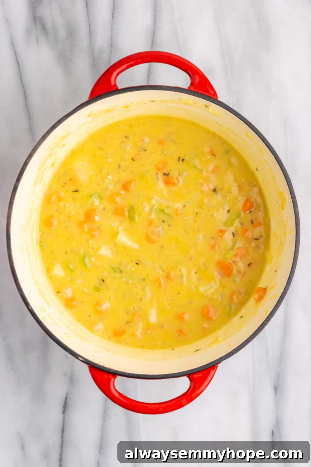 A Dutch oven containing a rich, creamy sauce with vegetables, after adding vegetable broth and vegan milk, ready for the final ingredients.