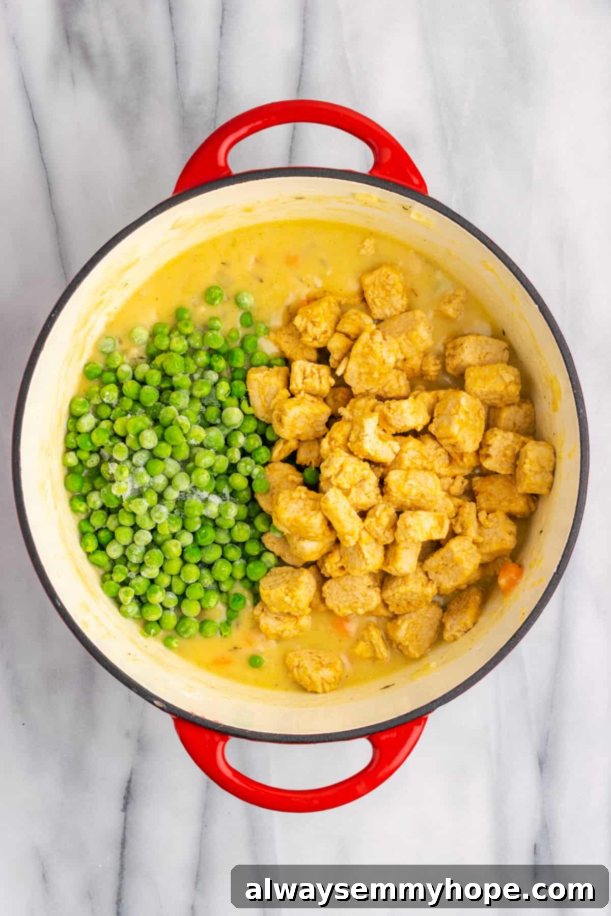Vegan chicken pieces and frozen green peas added on top of the creamy vegetable filling in a Dutch oven.