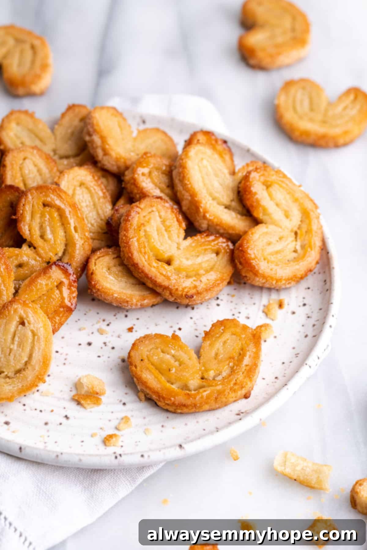 A plate with a pile of puff pastry palmiers, one palmier at the front, and lots of palmiers surrounding it
