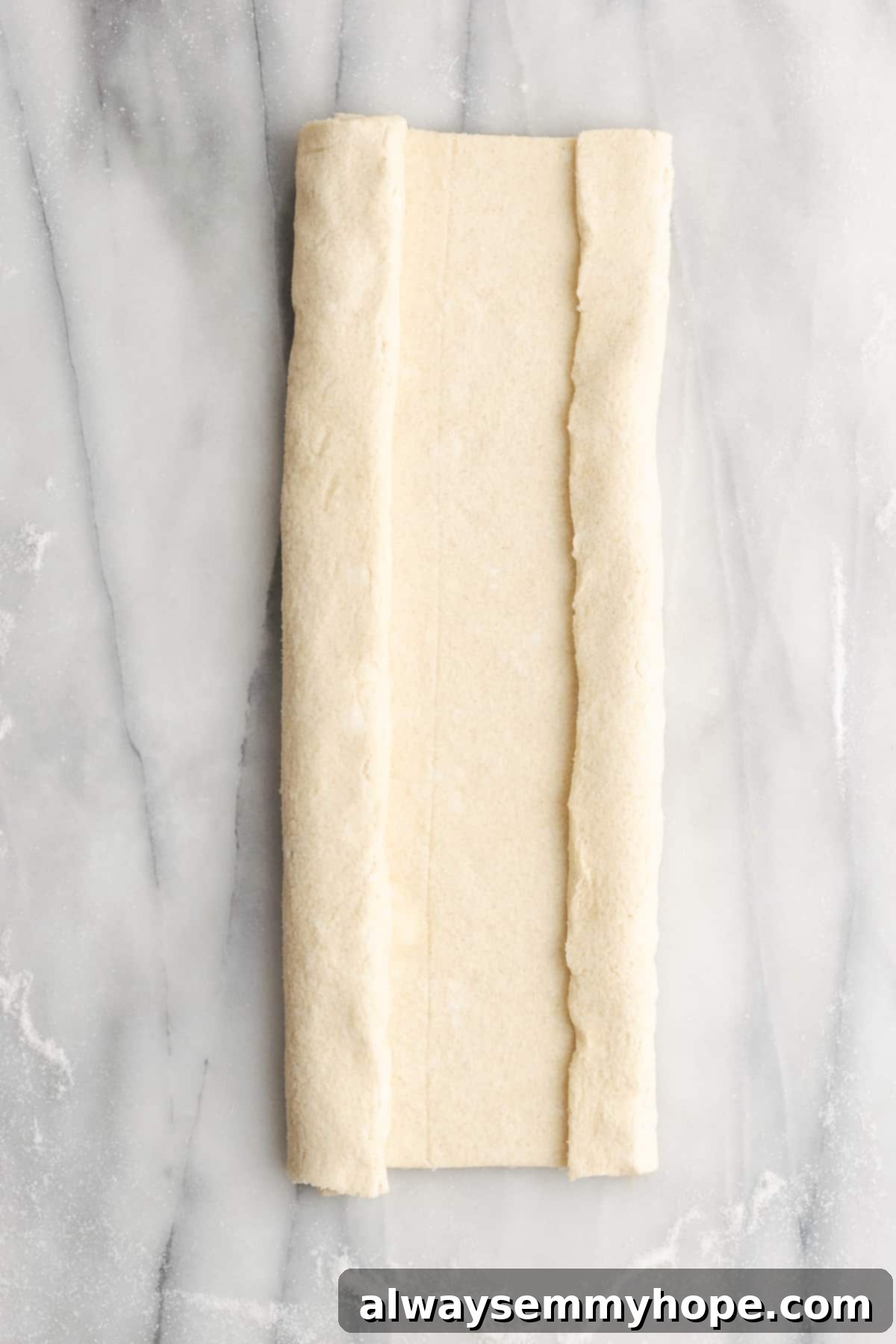 A rectangle of puff pastry dough with one side folded in about halfway, and the other about a quarter