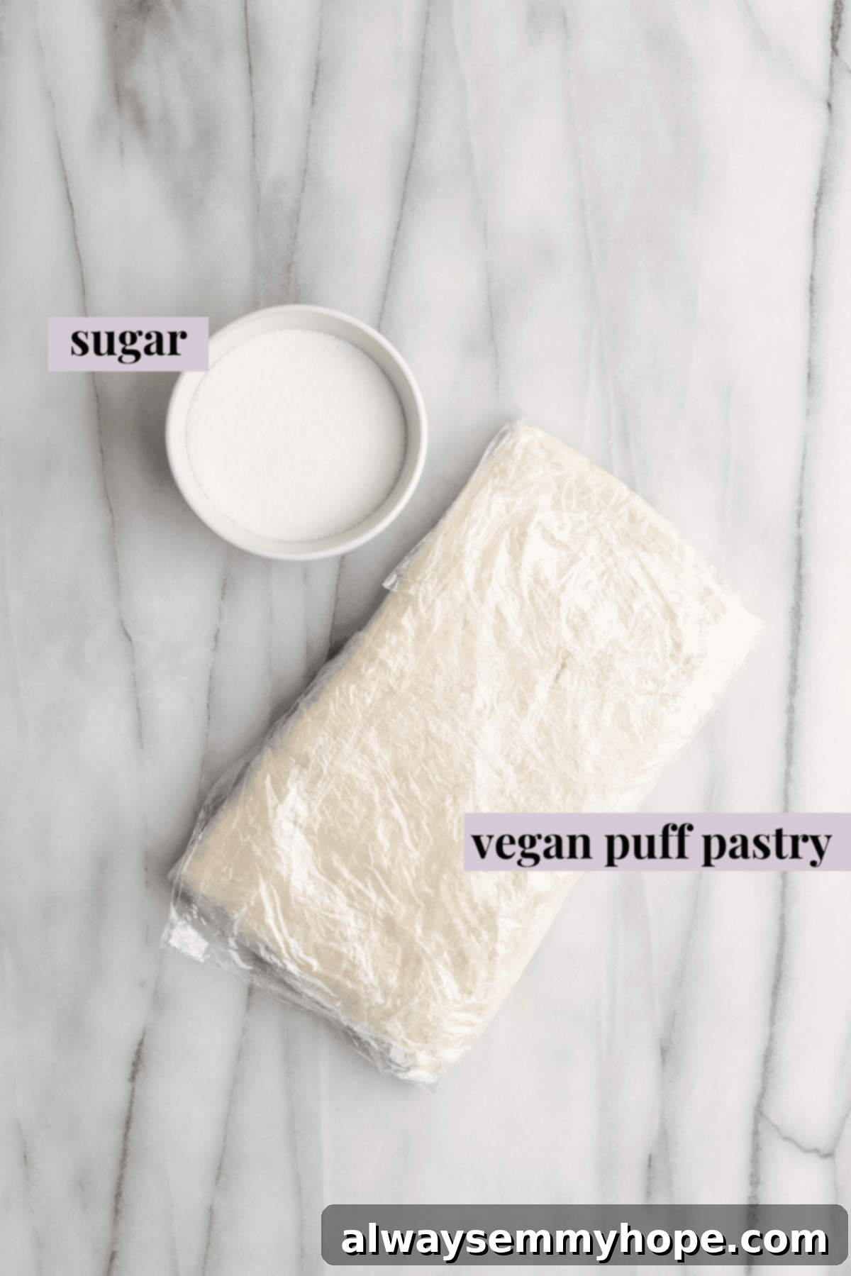 Overhead view of the labeled ingredients for vegan puff pastry palmiers: a bowl of sugar, and a piece of vegan puff pastry wrapped in plastic wrap