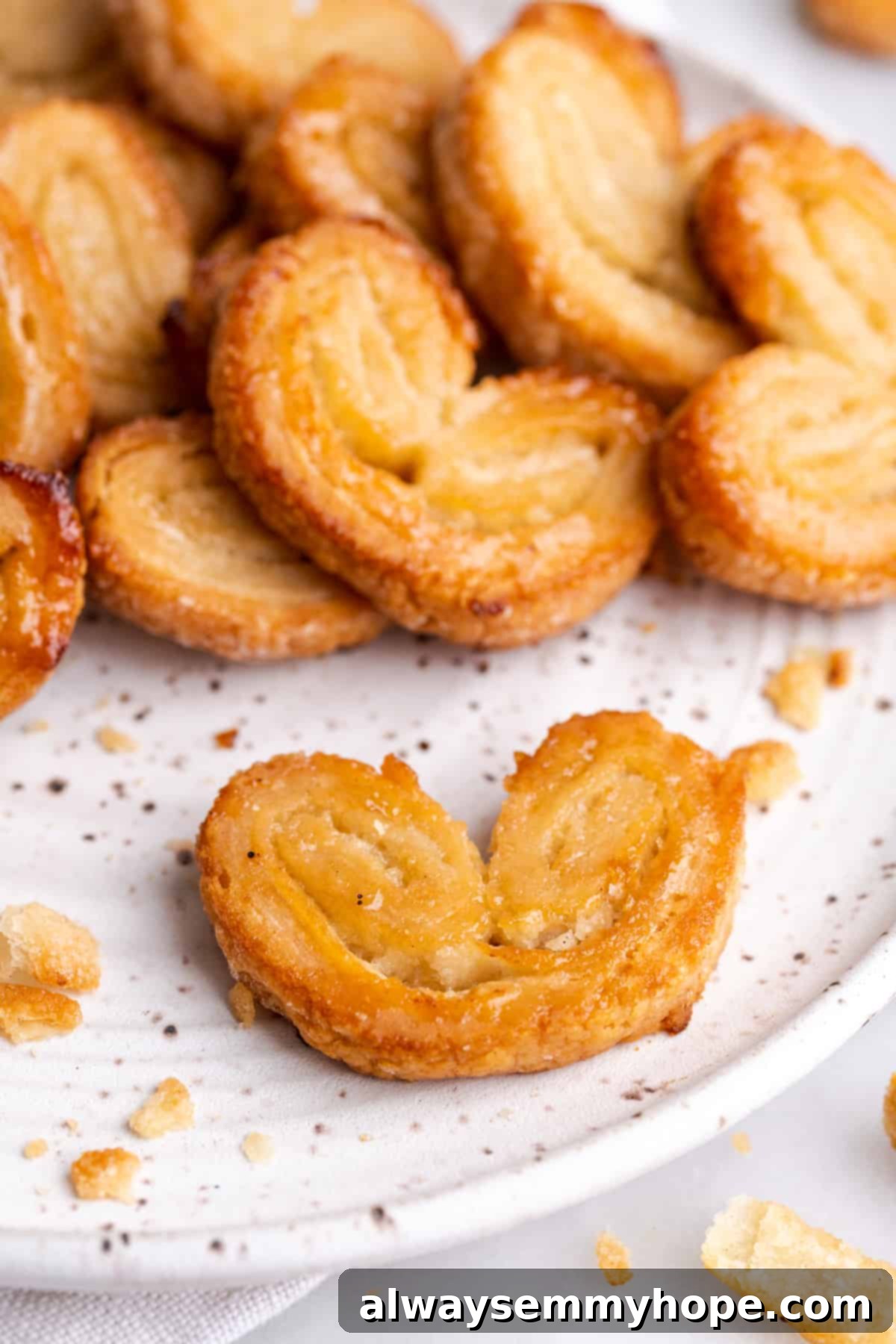 Close up of a puff pastry palmier on a plate, with a pile of palmiers behind it