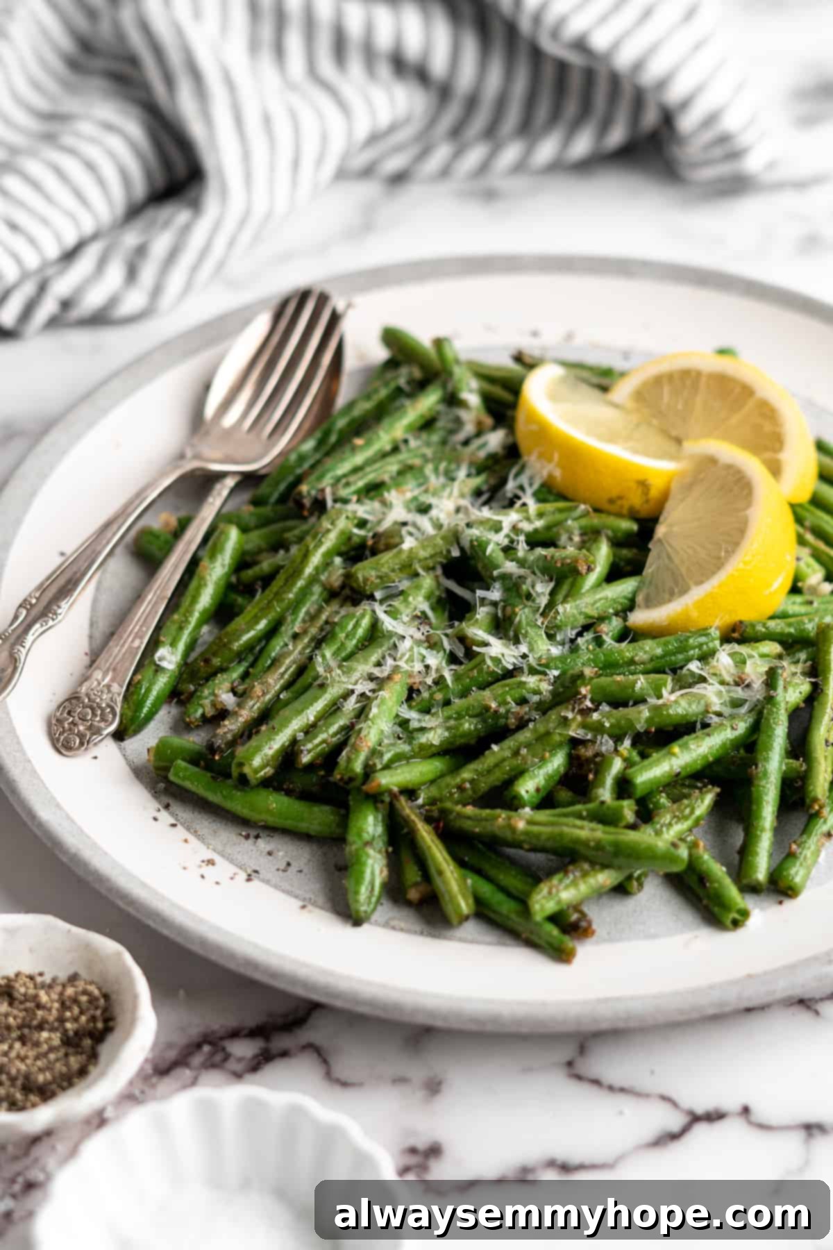 These air fryer green beans are seasoned to perfection and air fried until crispy for an easy side dish that goes with anything! Air fryer green beans on plate with spoon and fork, garnished with lemon wedges.