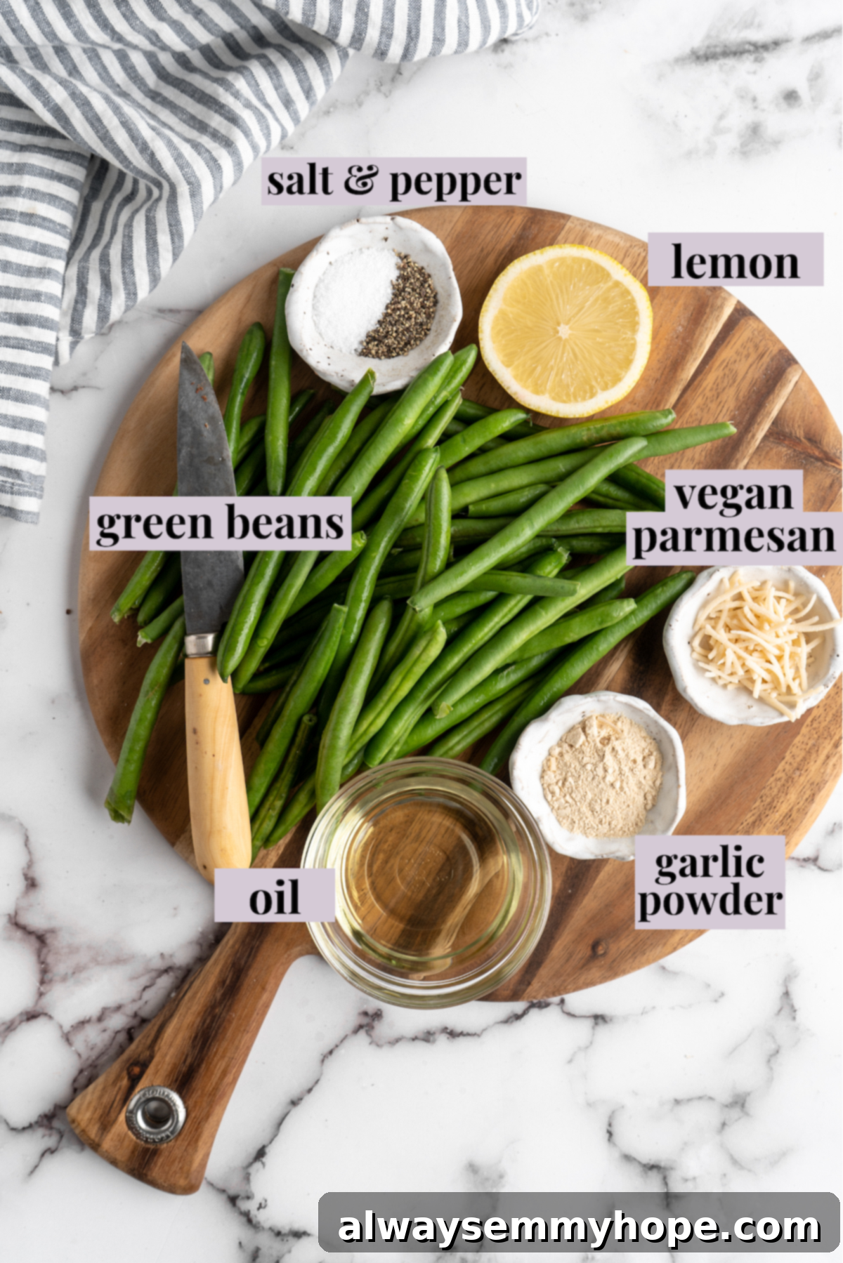 These air fryer green beans are seasoned to perfection and air fried until crispy for an easy side dish that goes with anything! Overhead view of air fryer green bean ingredients with labels, including fresh green beans, garlic powder, sea salt, black pepper, vegan Parmesan, lemon, and olive oil.