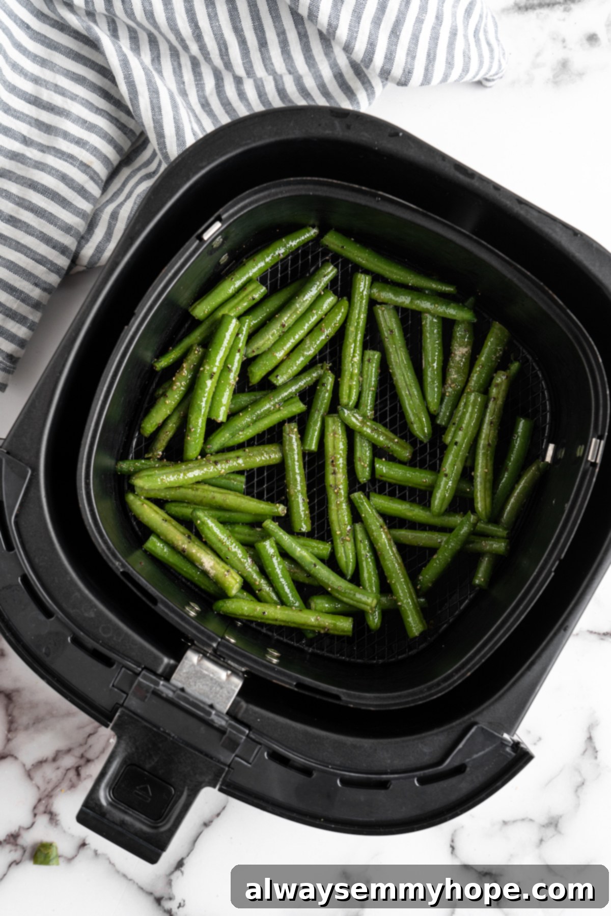 These air fryer green beans are seasoned to perfection and air fried until crispy for an easy side dish that goes with anything! Seasoned green beans laid out in a single layer in an air fryer basket, ready for cooking.