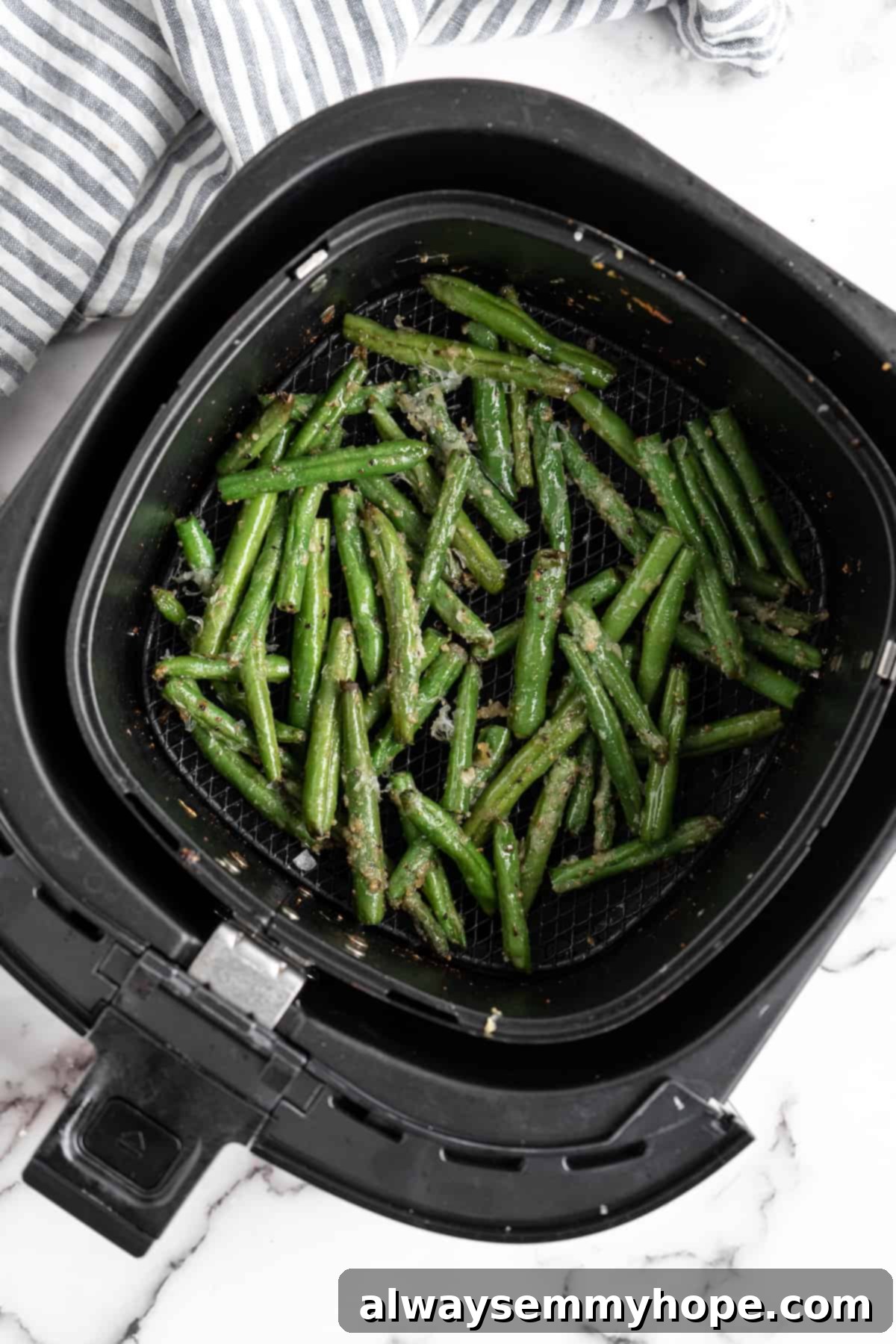 These air fryer green beans are seasoned to perfection and air fried until crispy for an easy side dish that goes with anything! Cooked air fryer green beans with vegan parmesan cheese inside the air fryer basket.