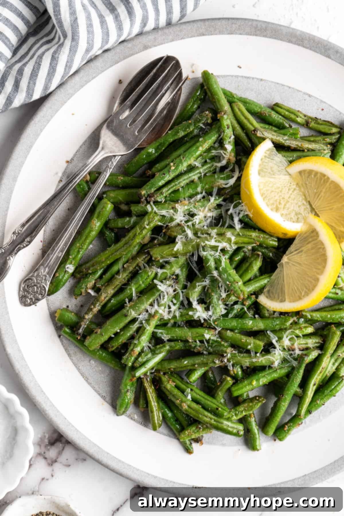 These air fryer green beans are seasoned to perfection and air fried until crispy for an easy side dish that goes with anything! Air fryer green beans on plate with spoon, fork, and lemon wedges, perfect as a healthy side dish.