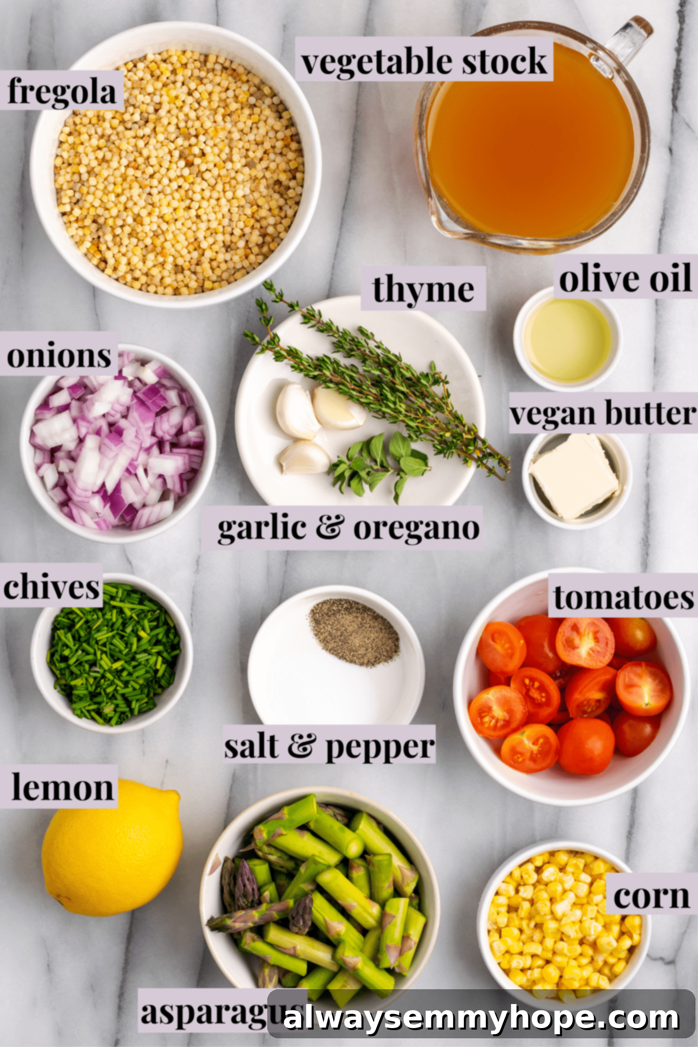An overhead shot showcasing fresh ingredients for Herb & Veggie Fregola, including vibrant asparagus, red onion, corn, garlic, and fresh herbs.