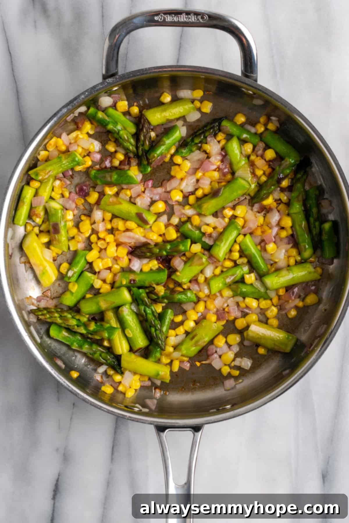 Red onions, chopped asparagus, and corn niblets sautéing in a skillet, creating a vibrant base for the fregola.