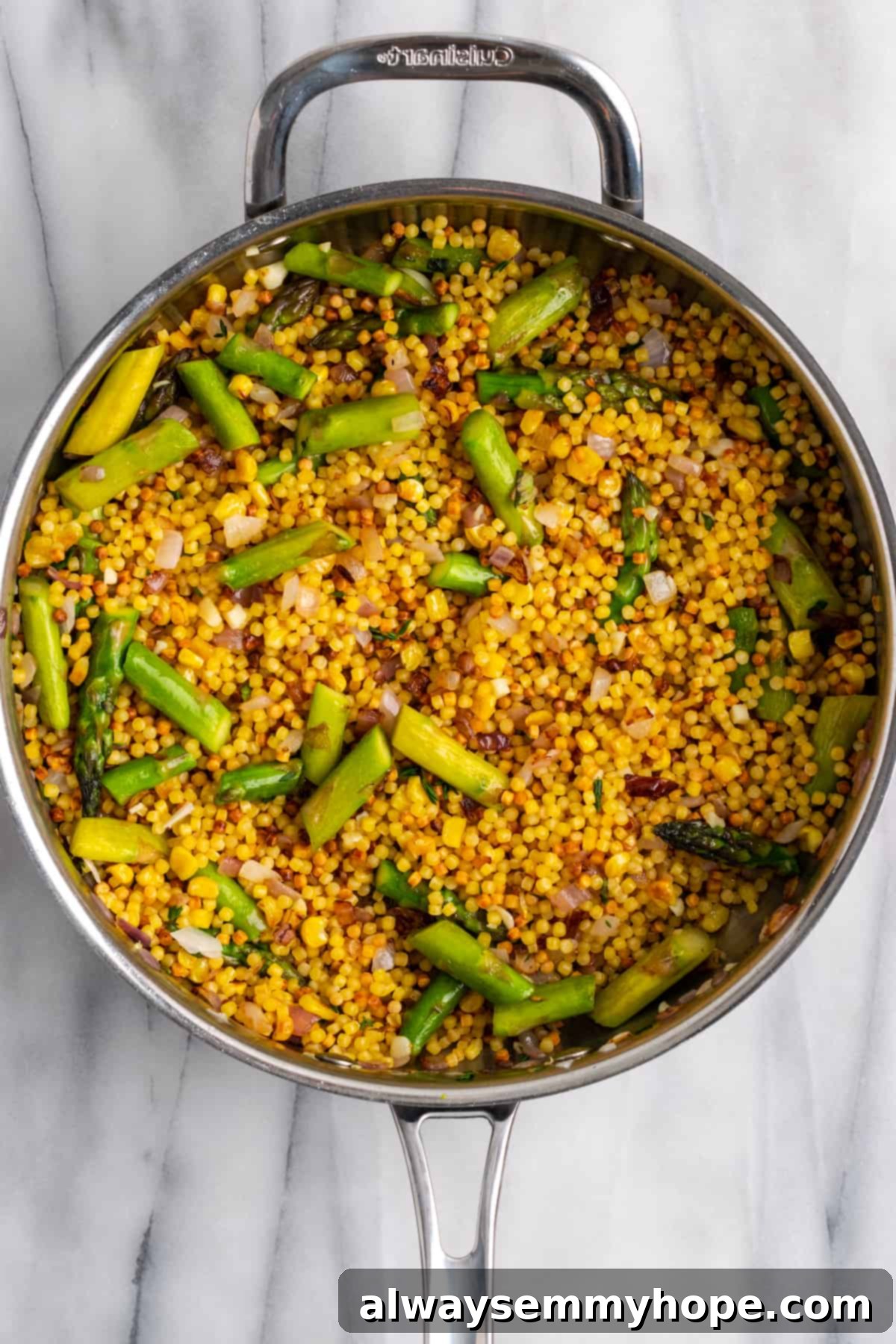 Toasting Fregola with Vegetables for Enhanced Flavor. Toasted fregola sarda pasta mixed with asparagus and other vegetables in a skillet, showcasing the golden-brown color achieved during the toasting process, ready for liquid addition.