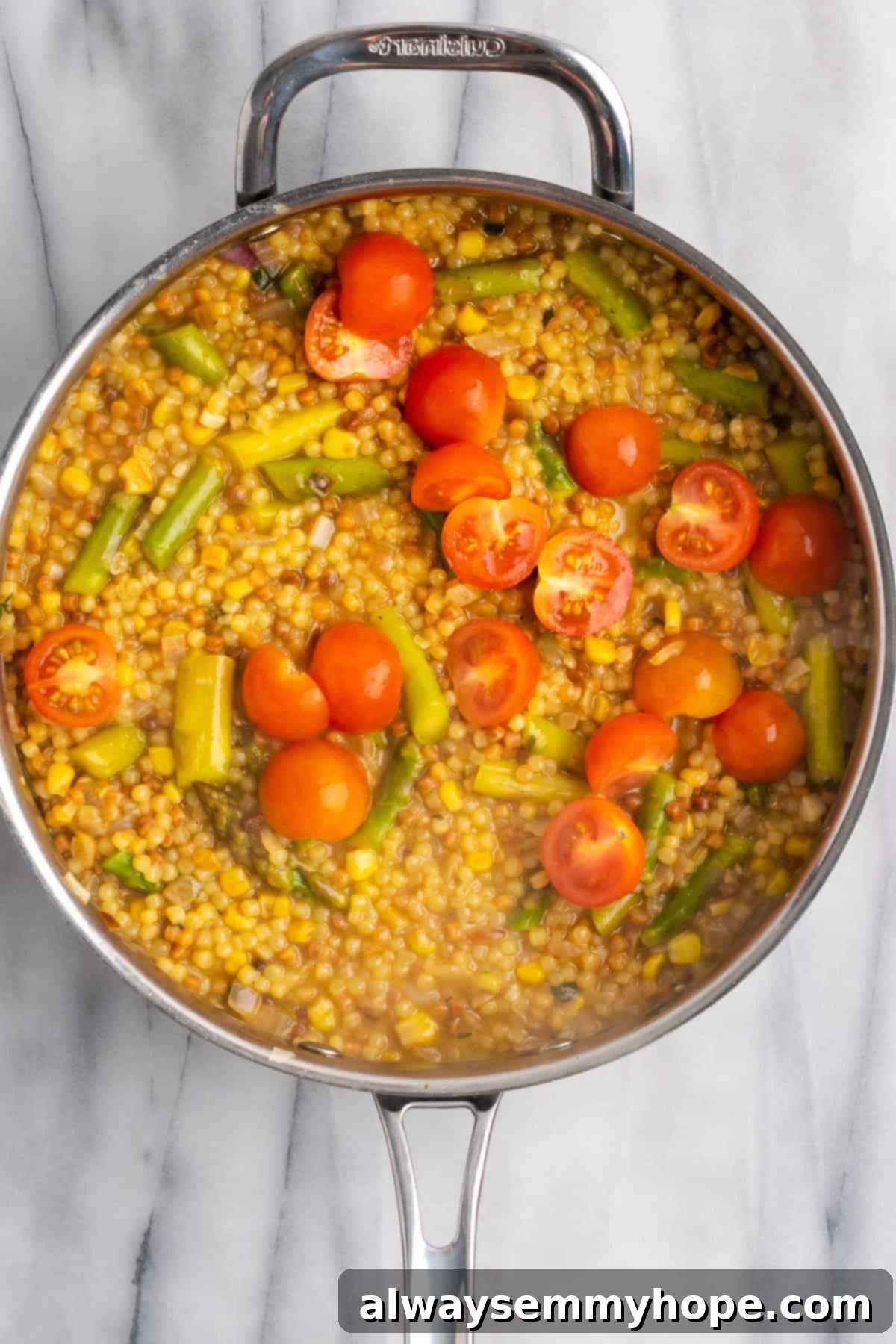 Adding Tomatoes to Cooked Fregola. Halved cherry tomatoes being stirred into the cooked fregola sarda and vegetable mixture in a skillet, adding fresh color and flavor.