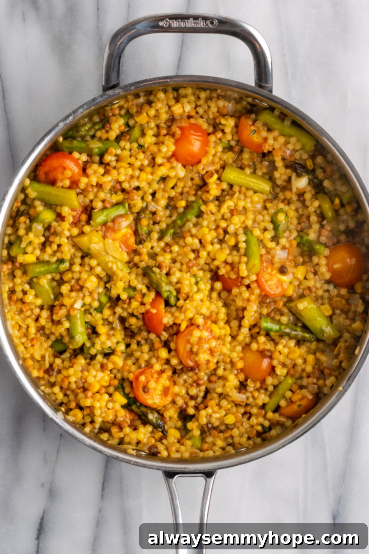 Finished Veggie Fregola Sarda in Skillet. Close-up overhead view of the finished Herb & Veggie Fregola in a skillet, showing the perfectly cooked pasta and vibrant vegetables coated in a light sauce.
