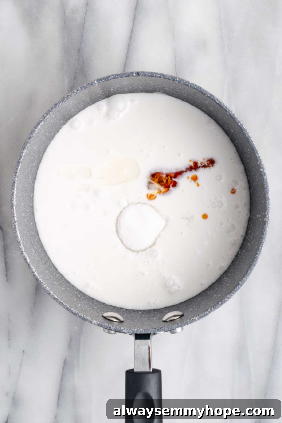 Hawaiian Coconut Haupia 6 A hand pouring cornstarch slurry into a pan of gently simmering haupia mixture, being whisked to combine.