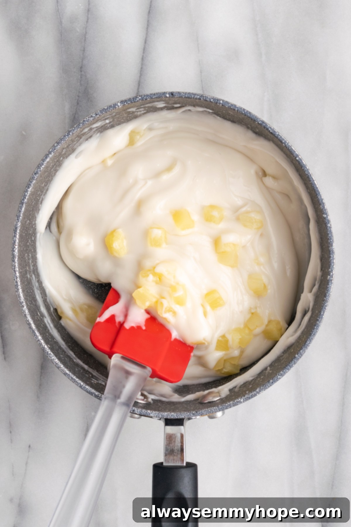 Hawaiian Coconut Haupia 10 A rubber spatula gently stirring the pineapple into the haupia mixture in the pan, ensuring even distribution.