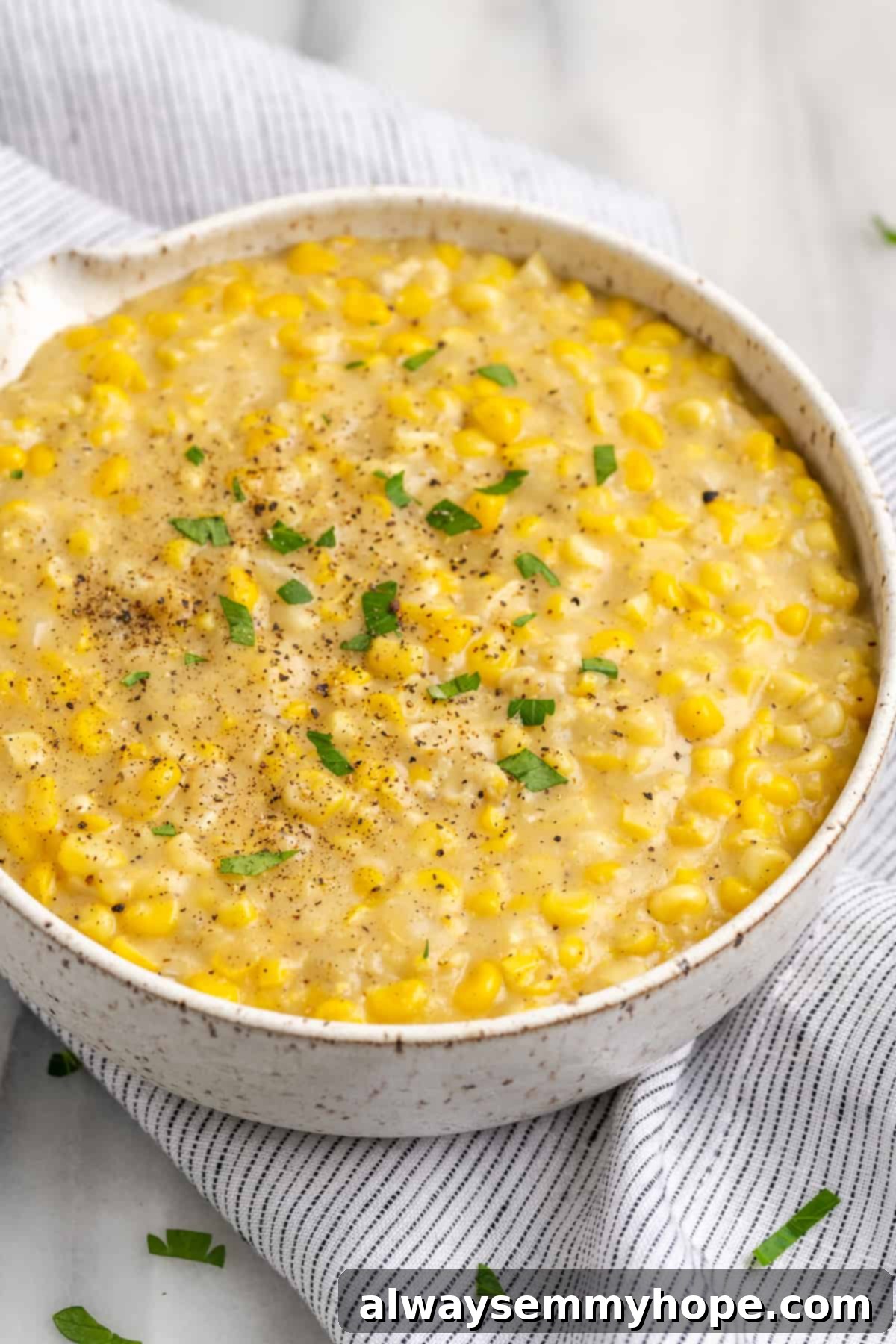 My recipe for vegan creamed corn is an easy way to make this crowd-pleasing side dish without the dairy milk and butter! Serving bowl of creamy vegan creamed corn on striped linen tablecloth