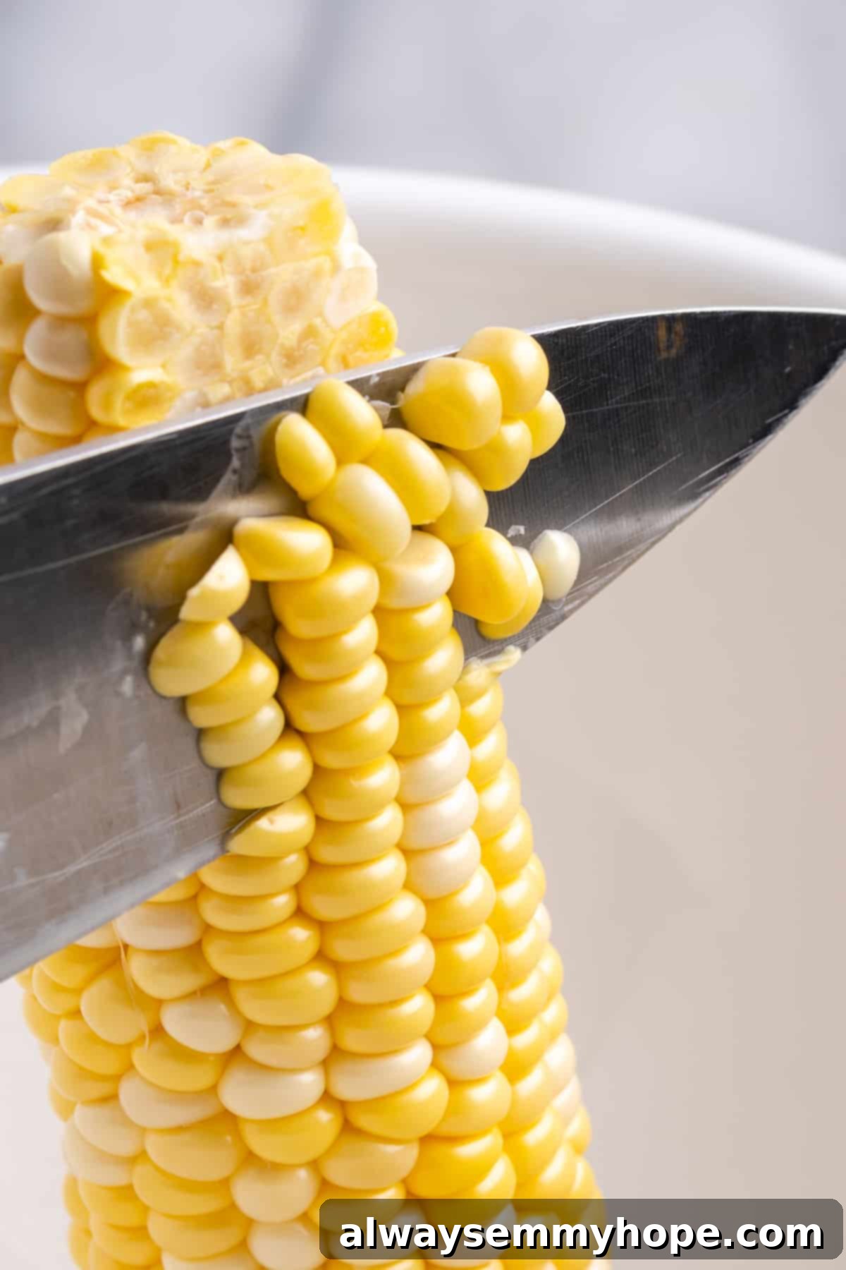 My recipe for vegan creamed corn is an easy way to make this crowd-pleasing side dish without the dairy milk and butter! Knife cutting kernels off a corn cob into a bowl