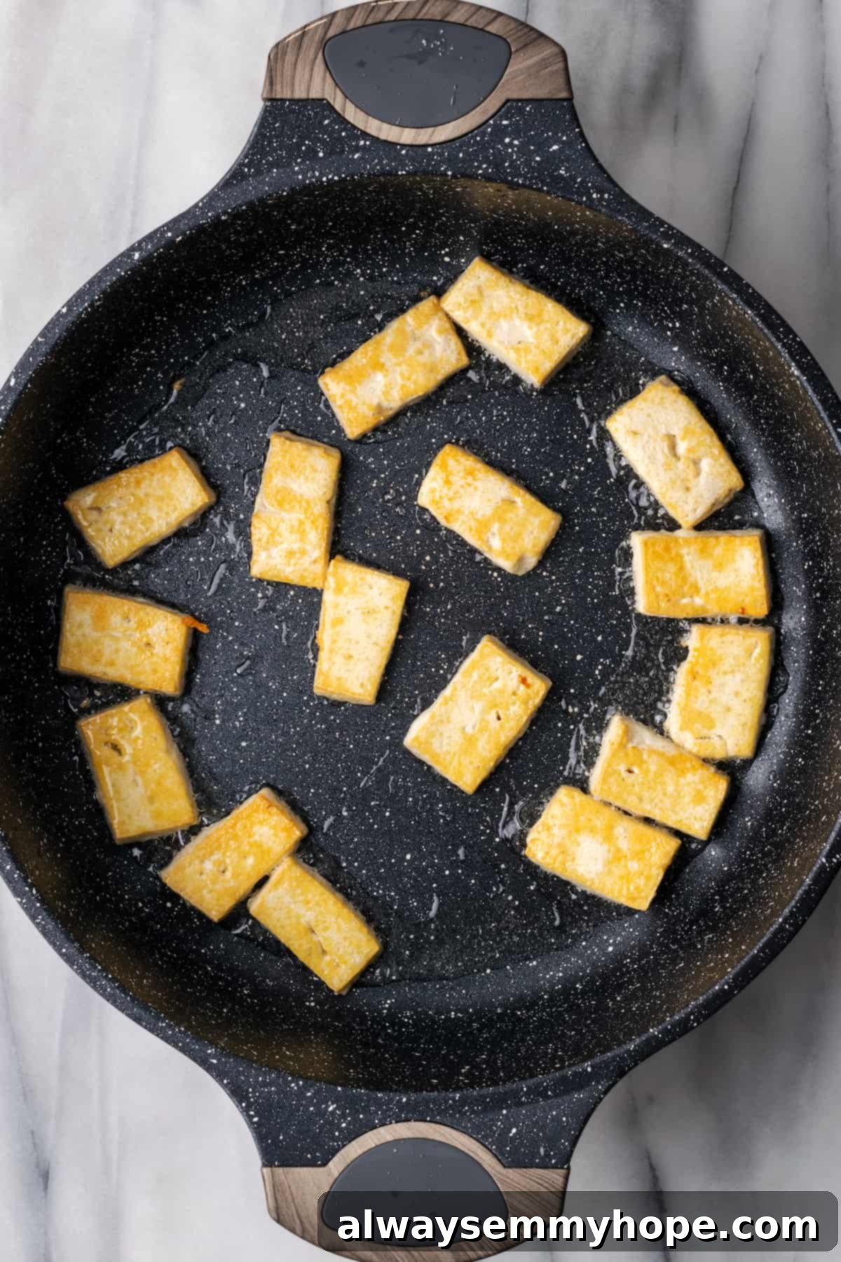 Golden perfection: Tofu cubes sizzling in the pan for a delightful texture in your vegan Chow Fun. Overhead view of firm tofu cubes cooking until golden brown in a hot pan.
