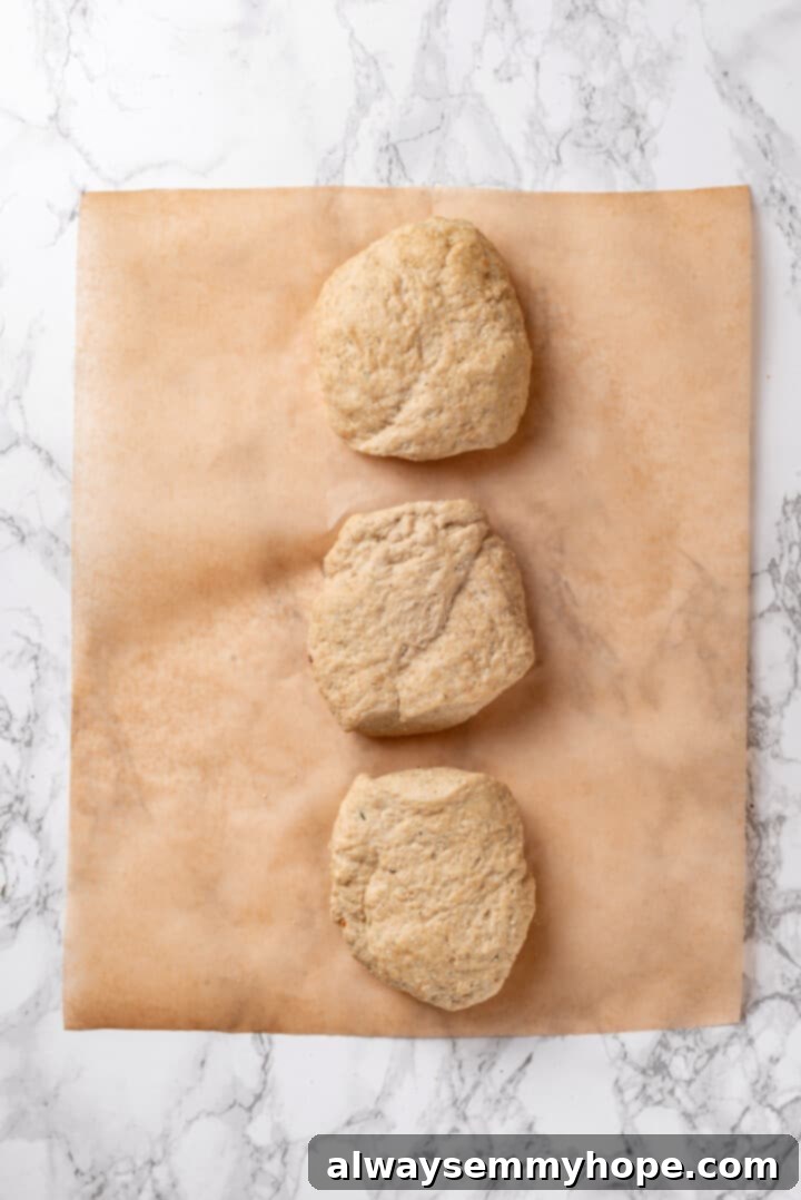 Three shaped vegan chicken breasts resting on parchment paper, prepared for steaming.