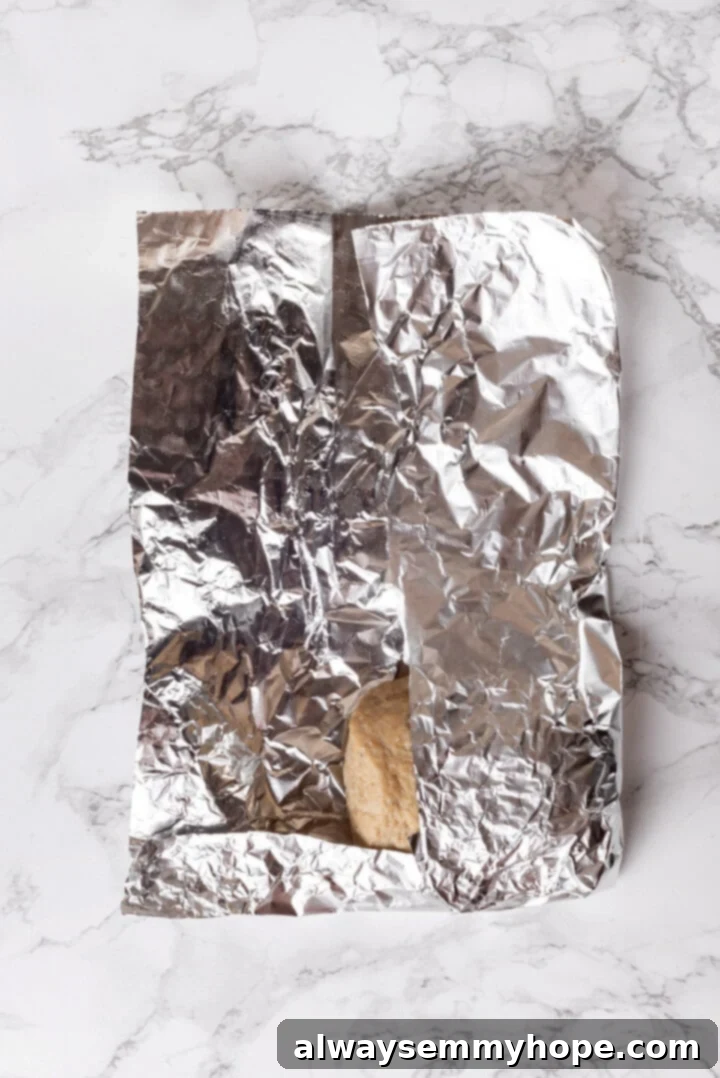 A vegan chicken piece being wrapped securely in aluminum foil, with sides folded inward.
