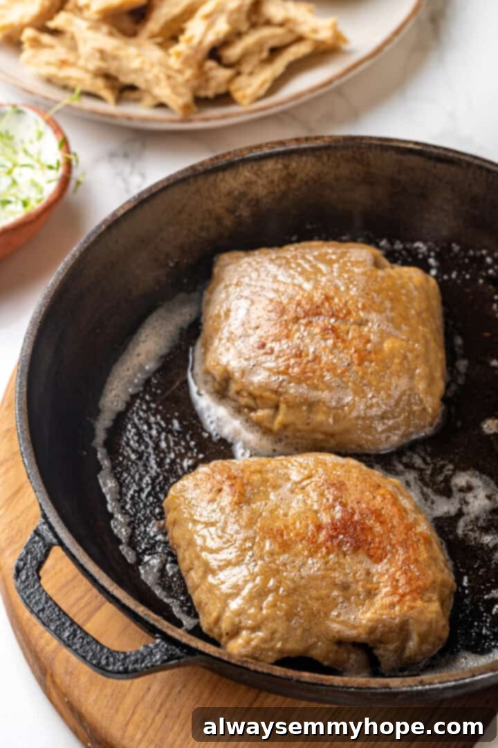 Two pieces of cooked vegan chicken browning in a cast iron skillet, showing the next step for preparing the chicken.