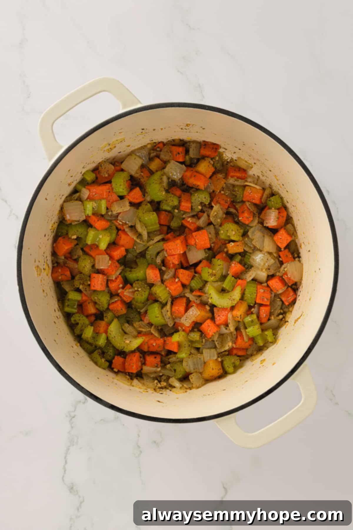 A colorful medley of cooked vegetables forming the base of the vegan chicken and dumplings stew. Overhead shot of perfectly sautéed onions, carrots, and celery in a large Dutch oven.