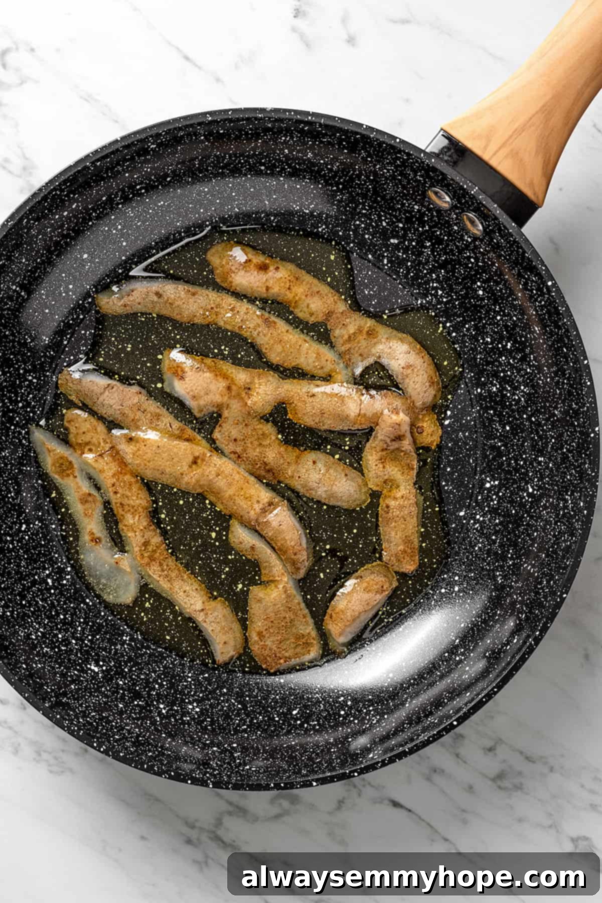 Overhead view of potato skins frying in a skillet until golden and crispy.