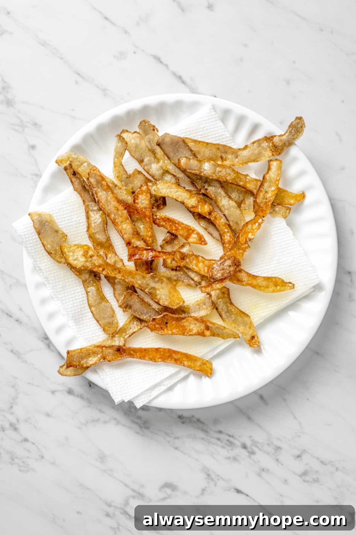 Crispy fried potato skins resting on a paper-towel-lined plate after frying.