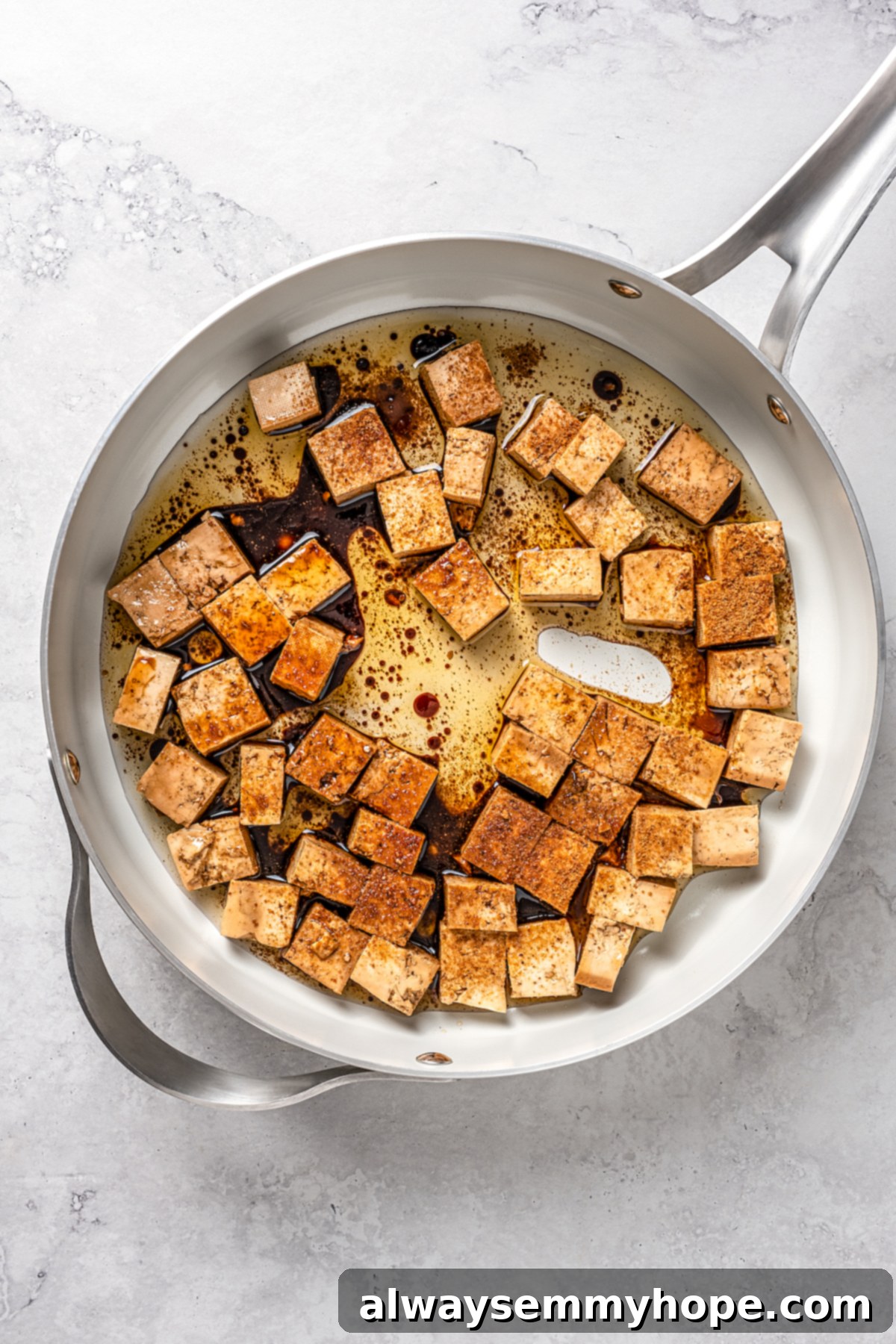 This vegan pad see ew pairs rice noodles, vegetables, and tofu with a sweet, savoury, and slightly tangy sauce for a restaurant-style meal! Overhead view of tofu slices cooking in a hot skillet, with some sauce beginning to caramelize.
