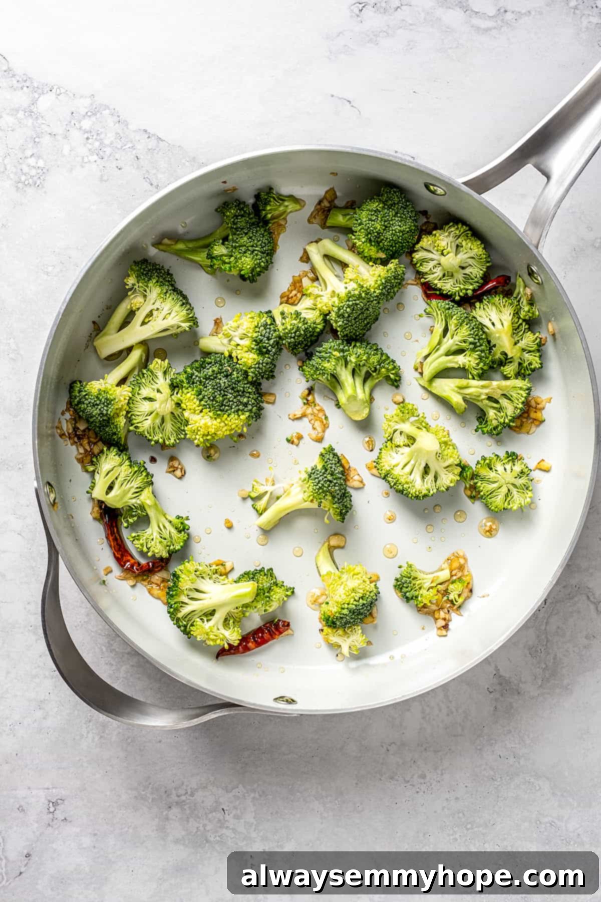 This vegan pad see ew pairs rice noodles, vegetables, and tofu with a sweet, savoury, and slightly tangy sauce for a restaurant-style meal! Overhead view of fresh broccoli florets added to the skillet with garlic and ginger, beginning to stir-fry.