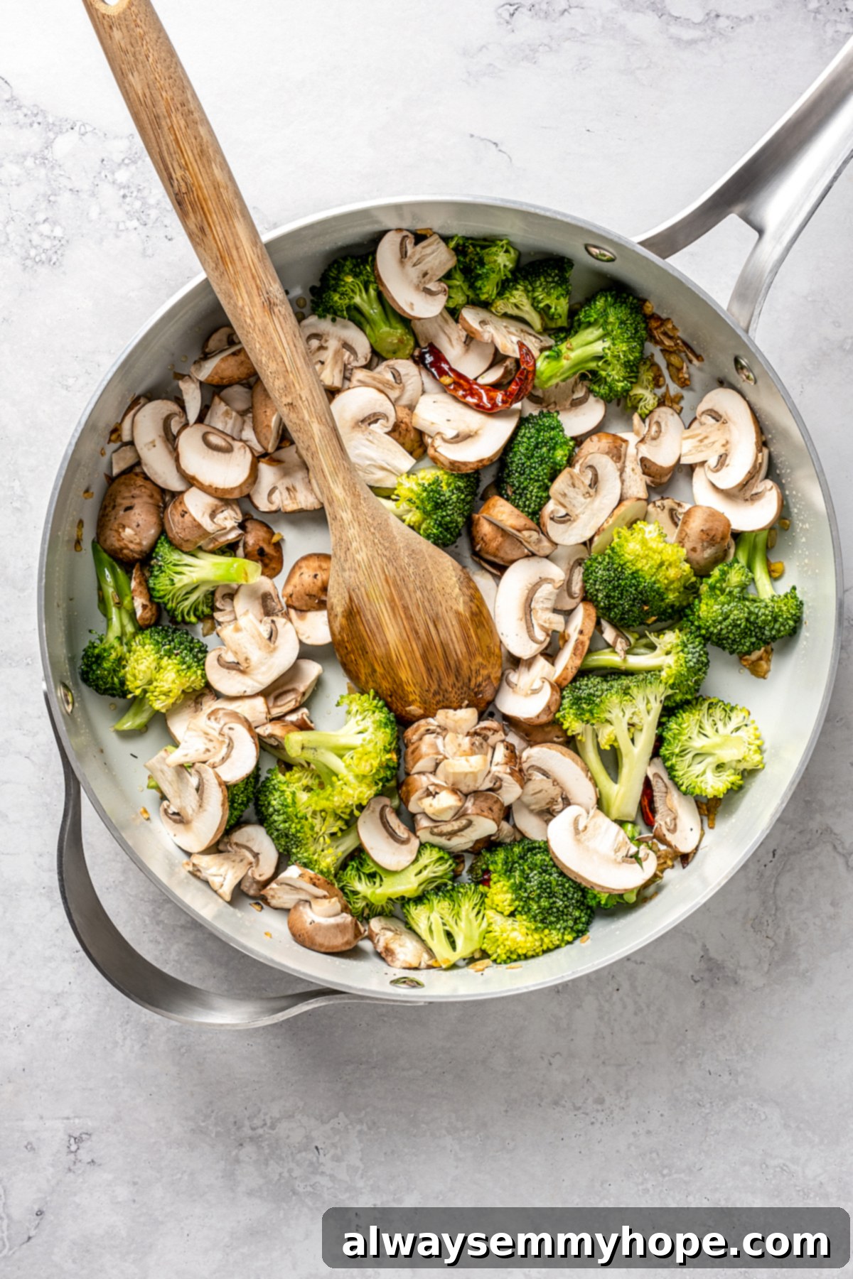 This vegan pad see ew pairs rice noodles, vegetables, and tofu with a sweet, savoury, and slightly tangy sauce for a restaurant-style meal! Overhead view of broccoli and sliced mushrooms stir-frying together in the skillet.
